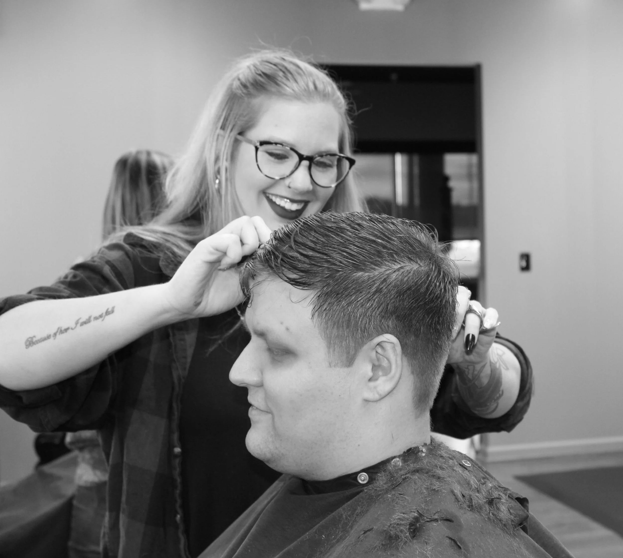 A person getting a haircut at a salon, with the barber using scissors in one hand and a clipper on the back of the person's head.