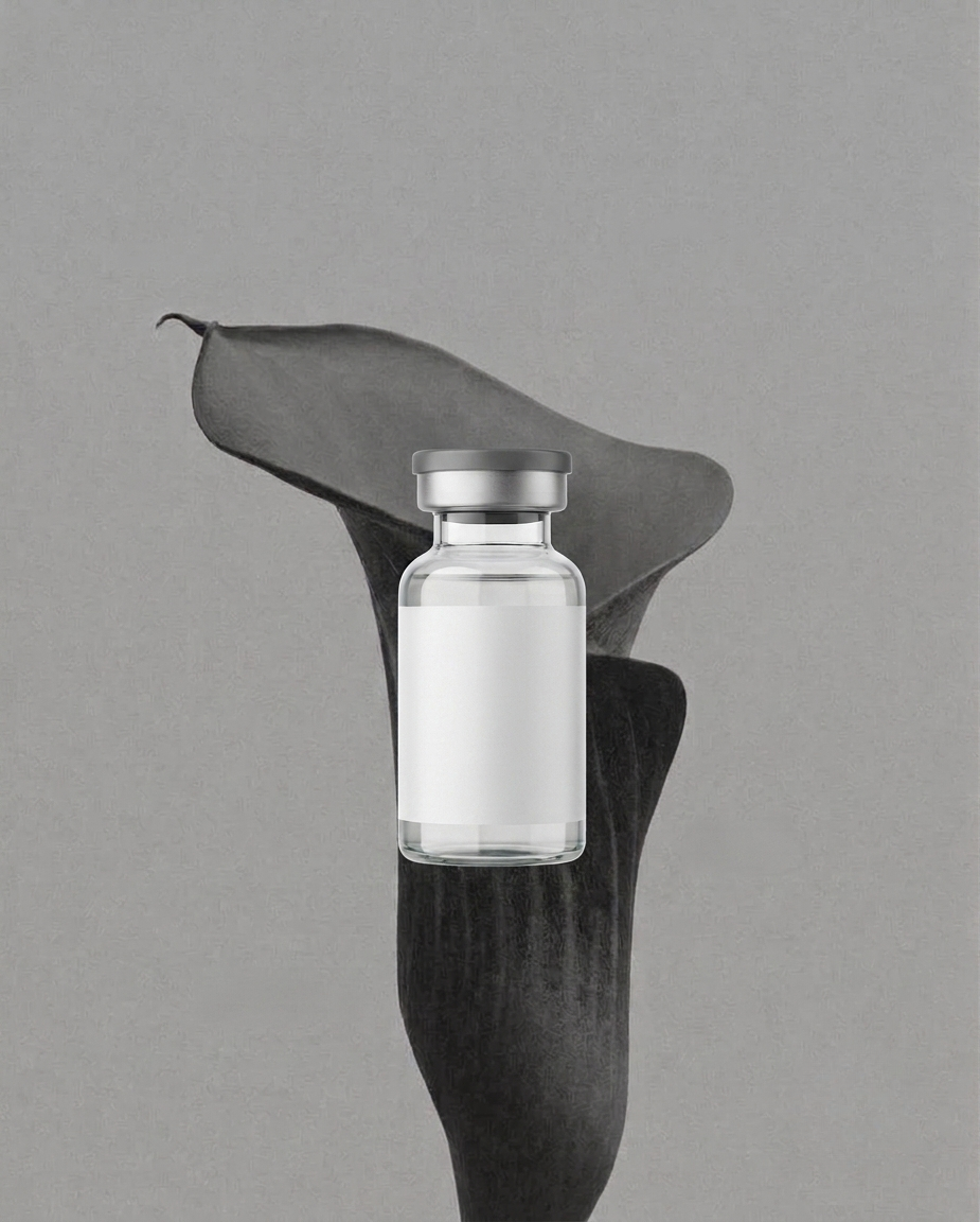 A small glass vial with a silver cap, filled with a clear liquid, is placed in front of a large black calla lily flower with a gray background.