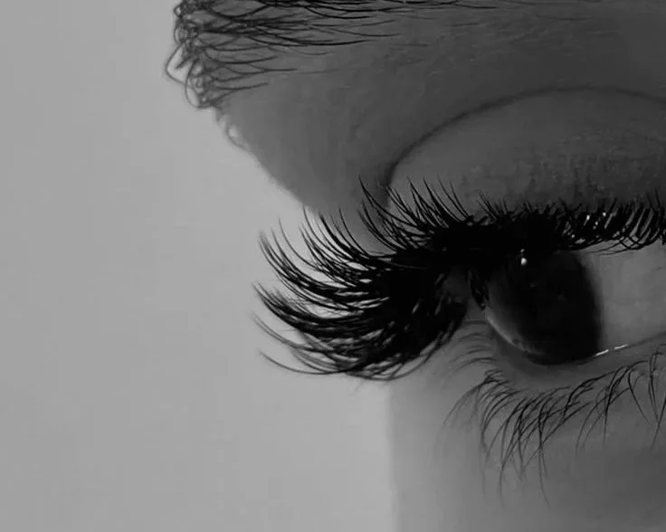 Close-up of a human eye with long eyelashes, shot in black and white.