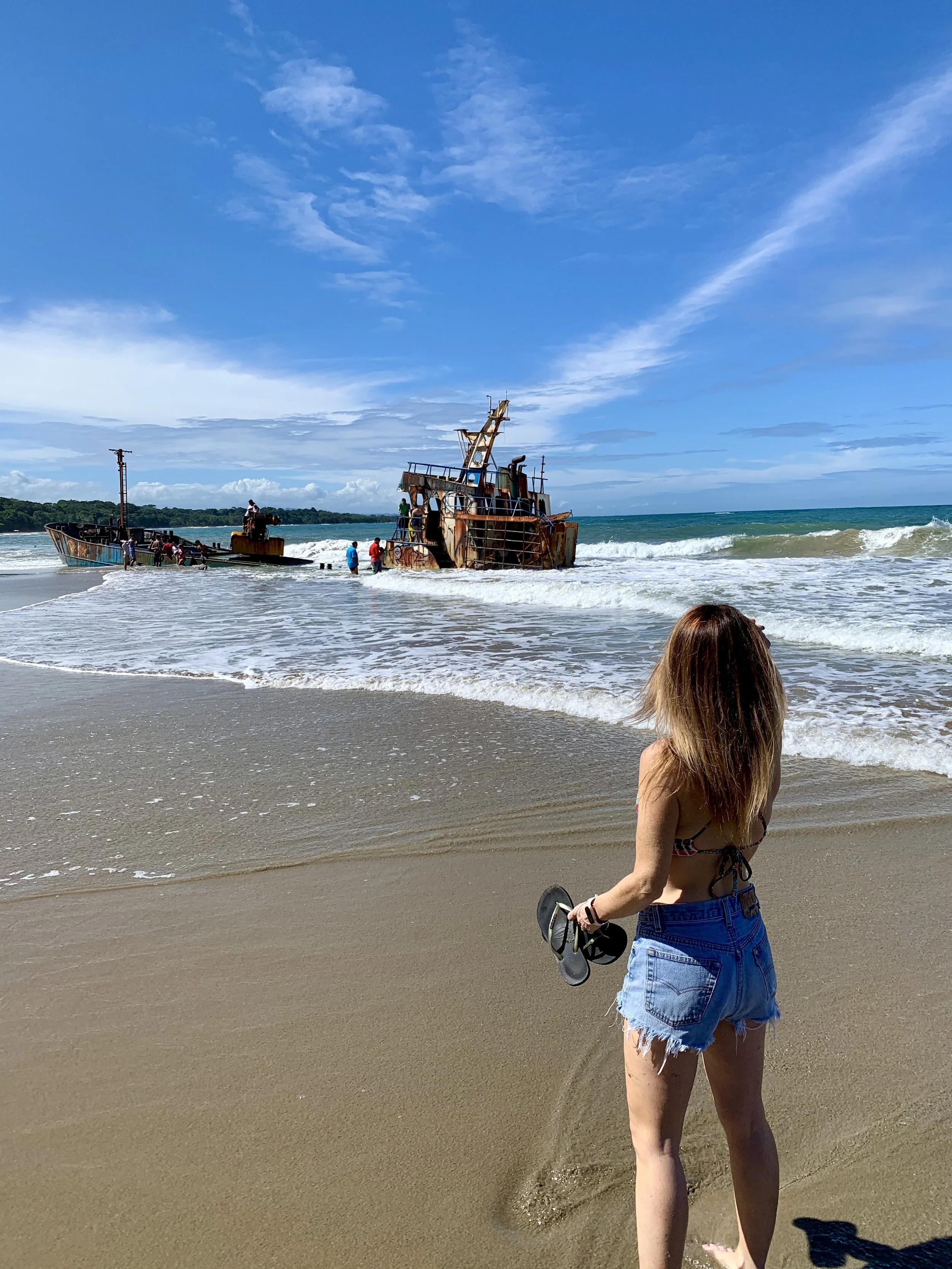 Raechelle standing on a beach in Costa Rica looking out at a ship beached just off the coastline.