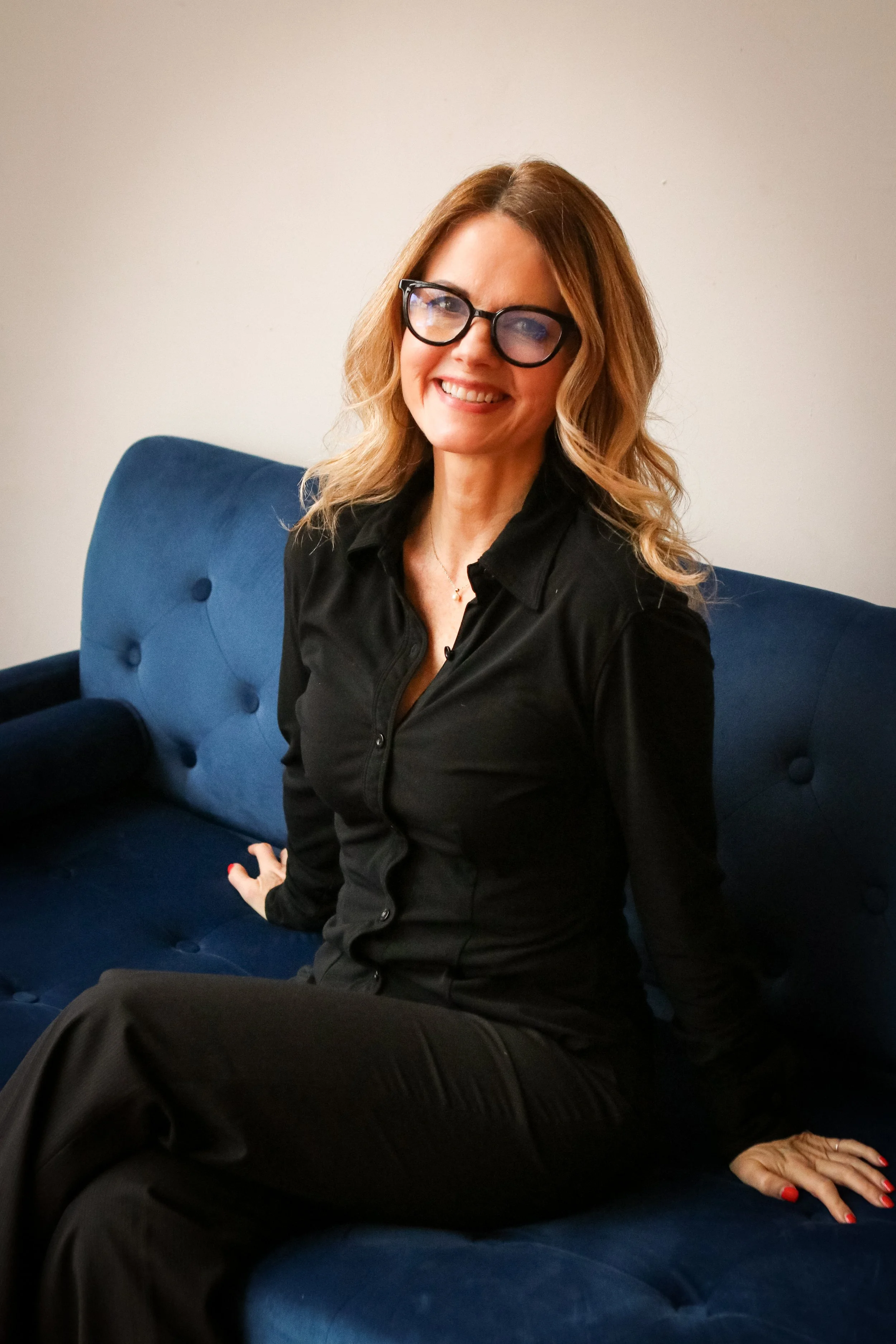 Raechelle smiling and sitting on a blue sofa.