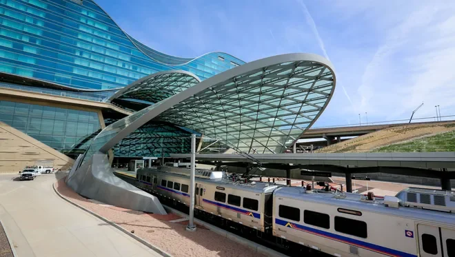 Modern train station with a sleek, curved glass roof and a passenger train stopped on the tracks outside.