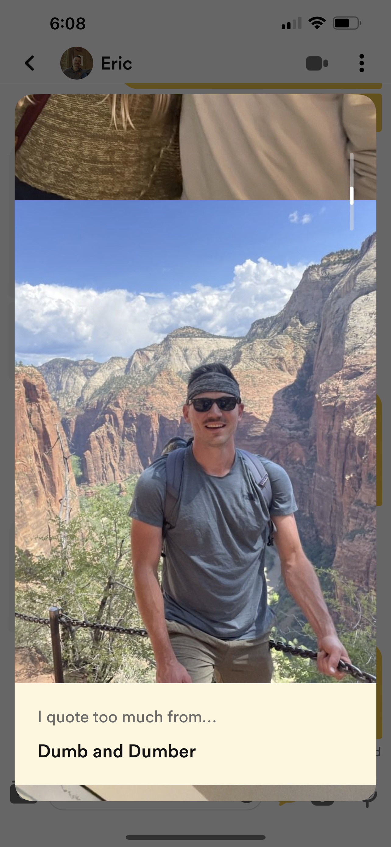 A man in sunglasses, a headband, and a gray t-shirt stands on a trail with a canyon landscape in the background, smiling at the camera.