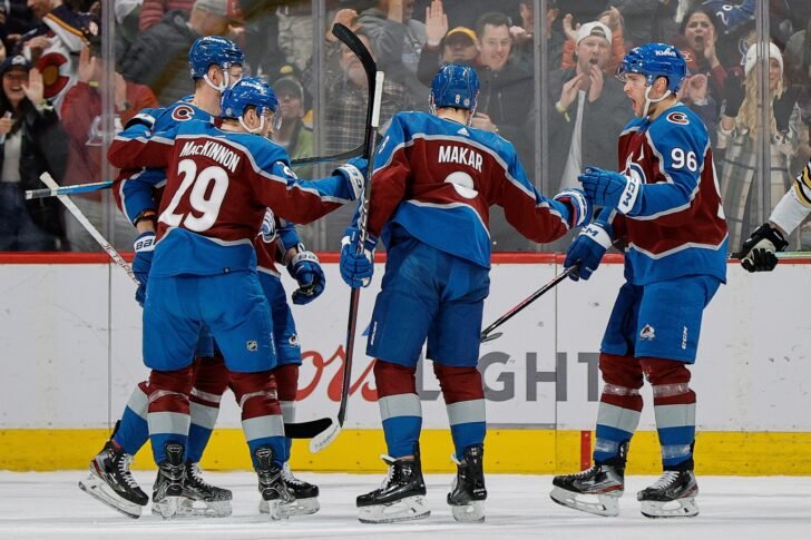 A team of hockey players in maroon and blue uniforms celebrating on the ice rink, with spectators cheering in the background.