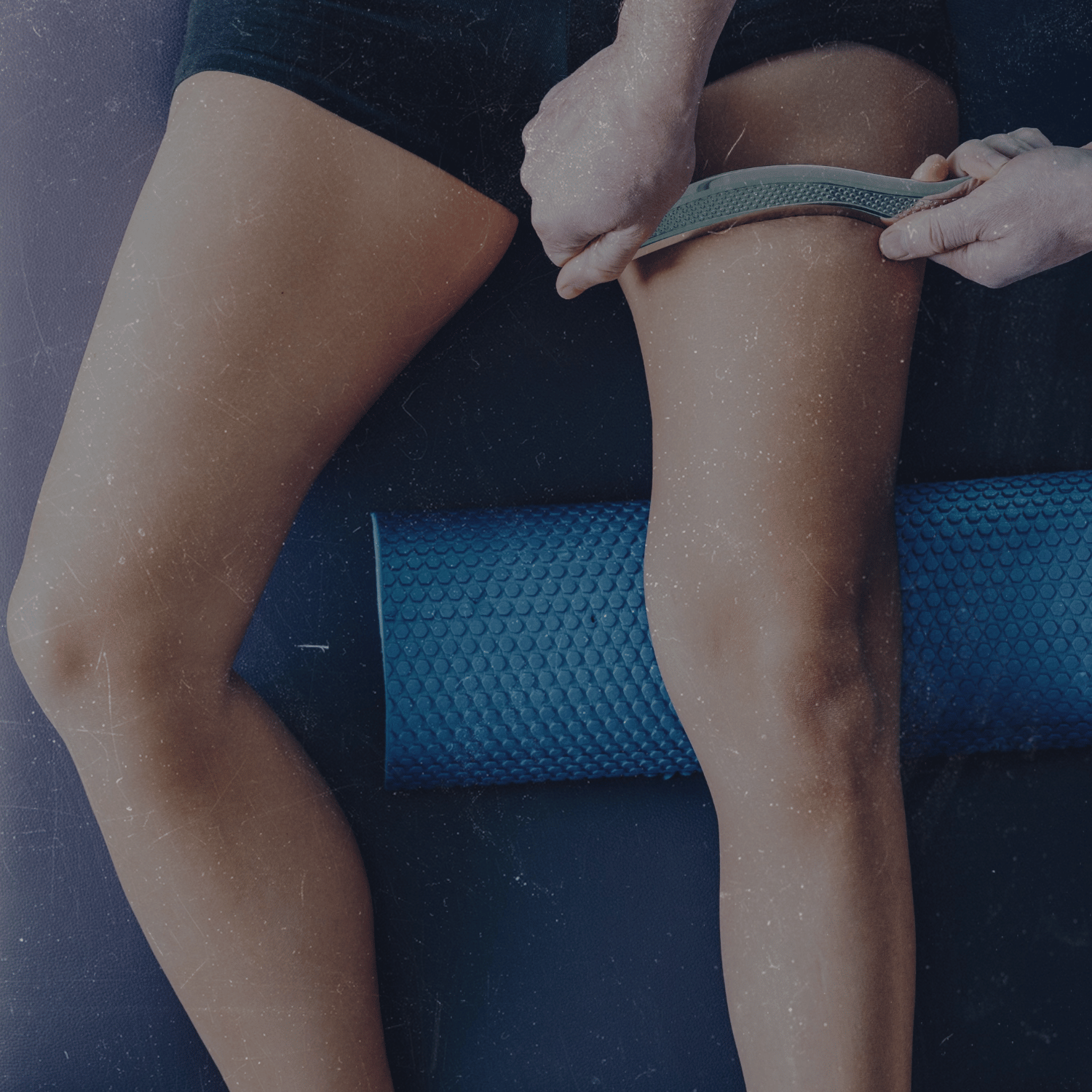 Close-up of a person stretching with a foam roller on their thighs, sitting on a dark surface.