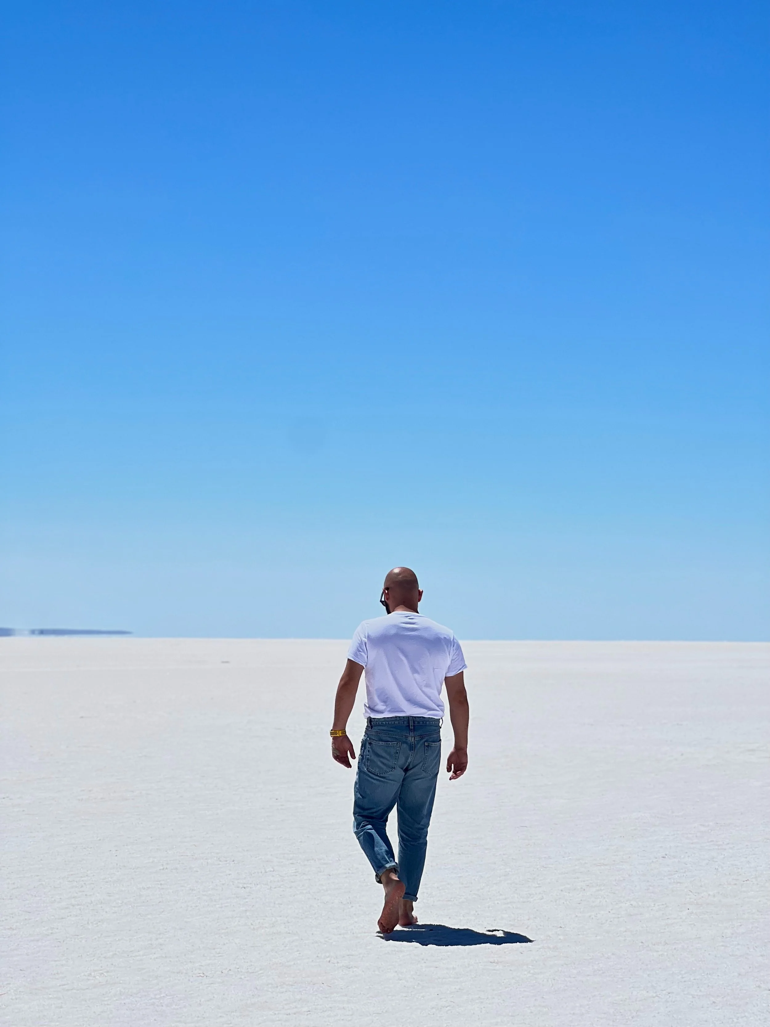 Man walking barefoot on a white desert with clear blue sky overhead