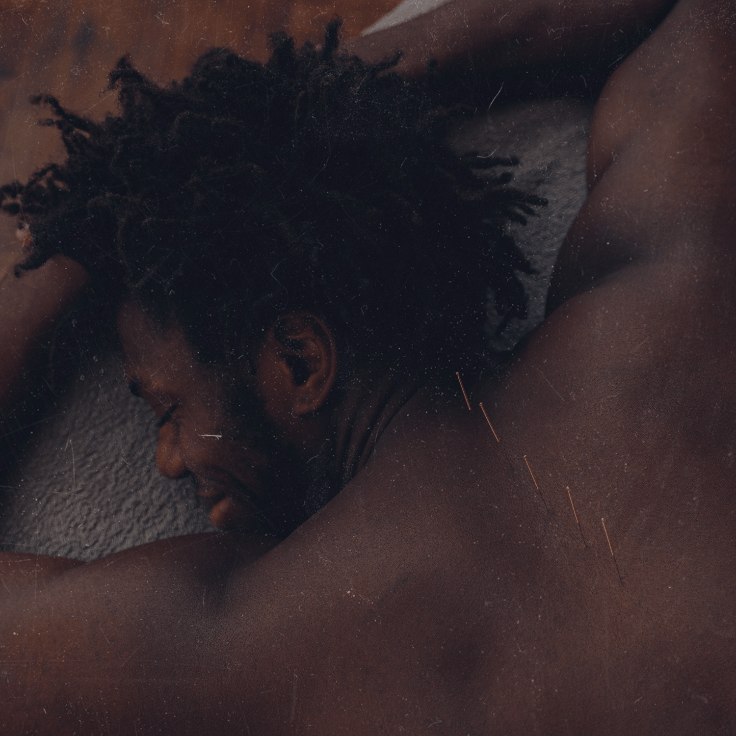 A person with dreadlocks is lying face down on a textured surface, appearing relaxed or resting.