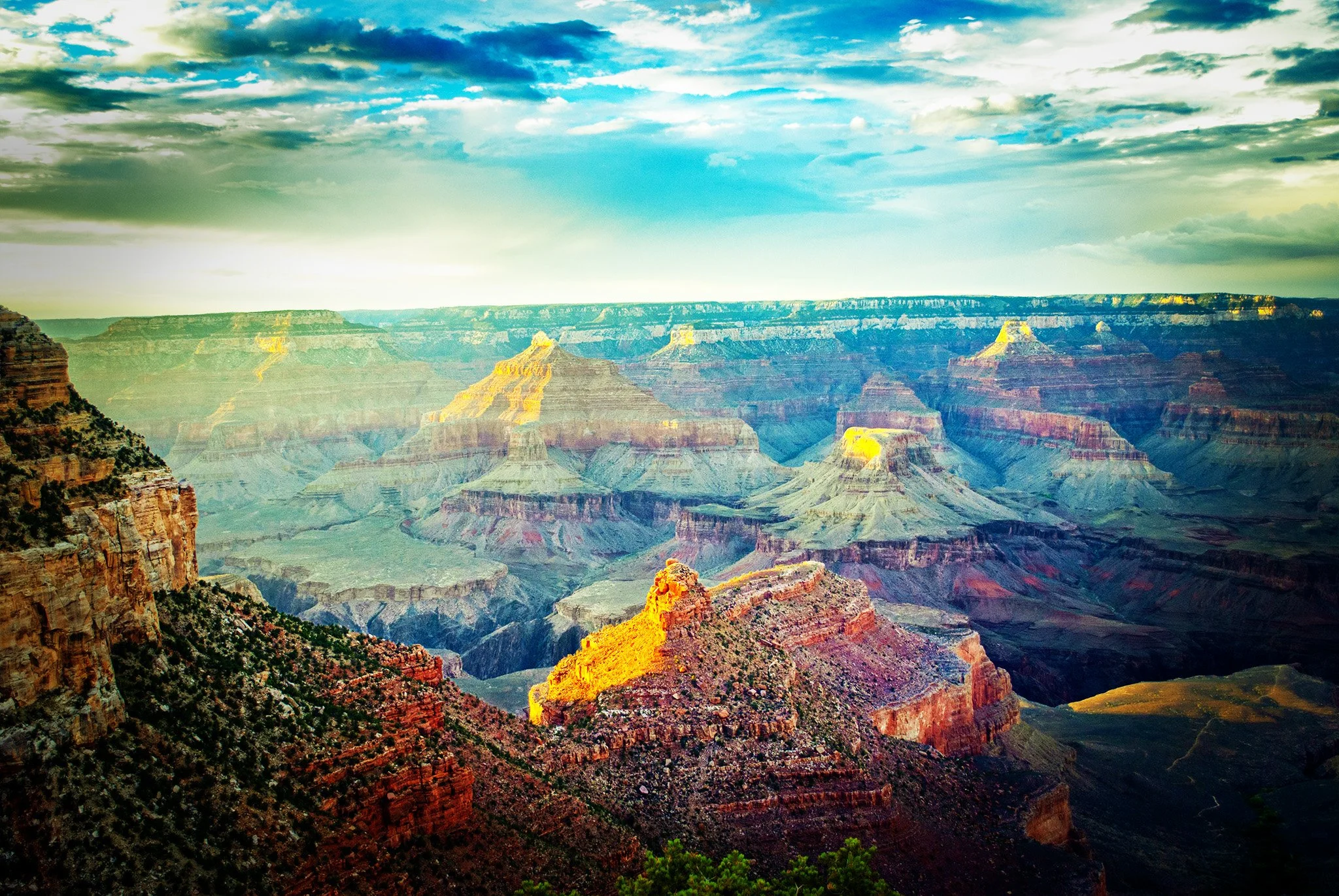 Colorful view of the Grand Canyon during daytime with layered red and green rock formations and a partly cloudy sky.