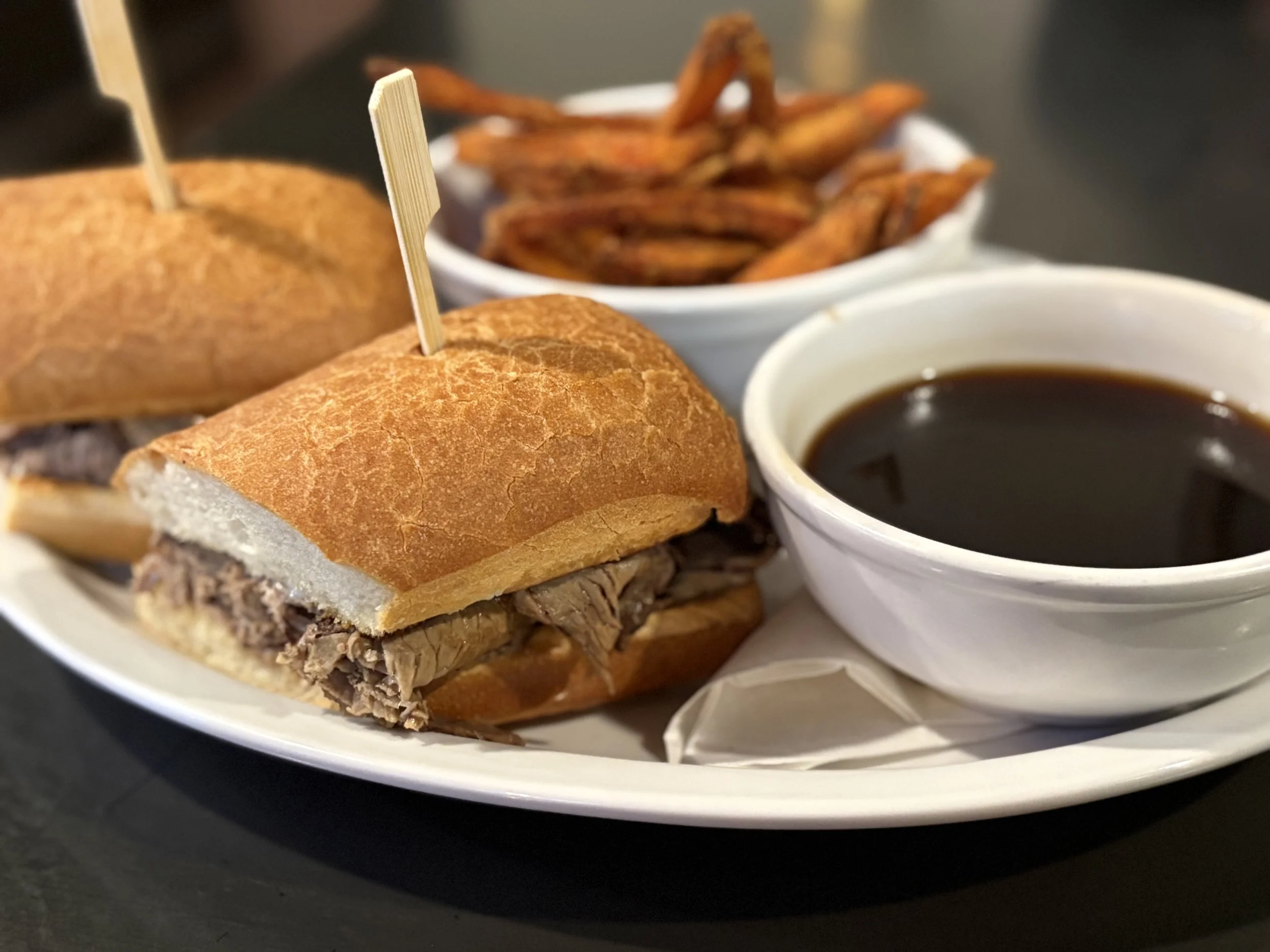 Beef dip sandwich with au jus sauce and side of sweet potato fries.