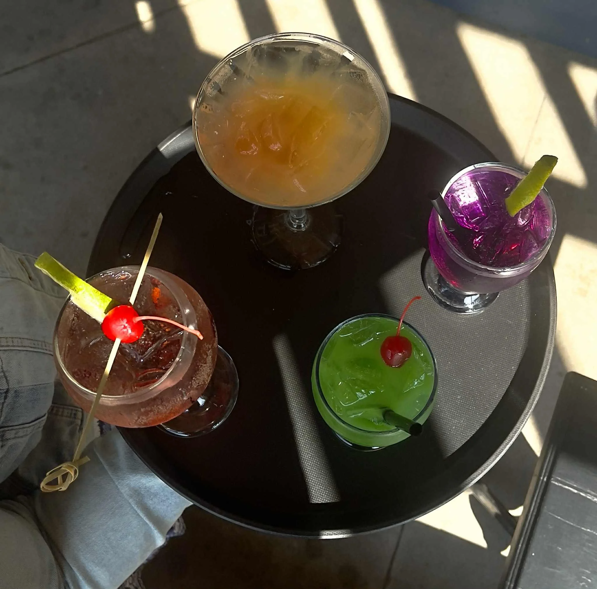 A serving tray full of colurful cocktails ready to be served on the Historic Salmo Hotel patio. There is a wine spritzer, a blue hawaiian, a Gin and Tonic, and a Beachcomber.