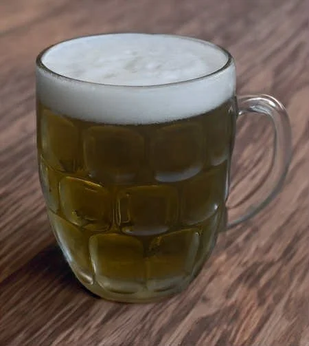 A beer with a nice one inch head sits on a wood grain table in The Historic Salmo Hotel in Salmo BC Beer on tap draught craft