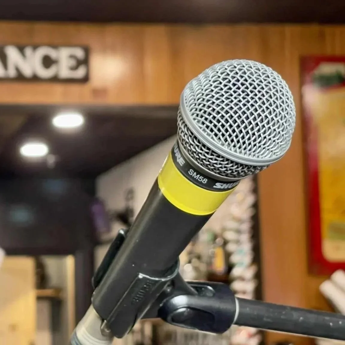 A silver microphone with a yellow tape band sits in the foreground. In the background, a wooden pub entrance sign is illuminated by potlights. A keno lottery machine sits in the background.