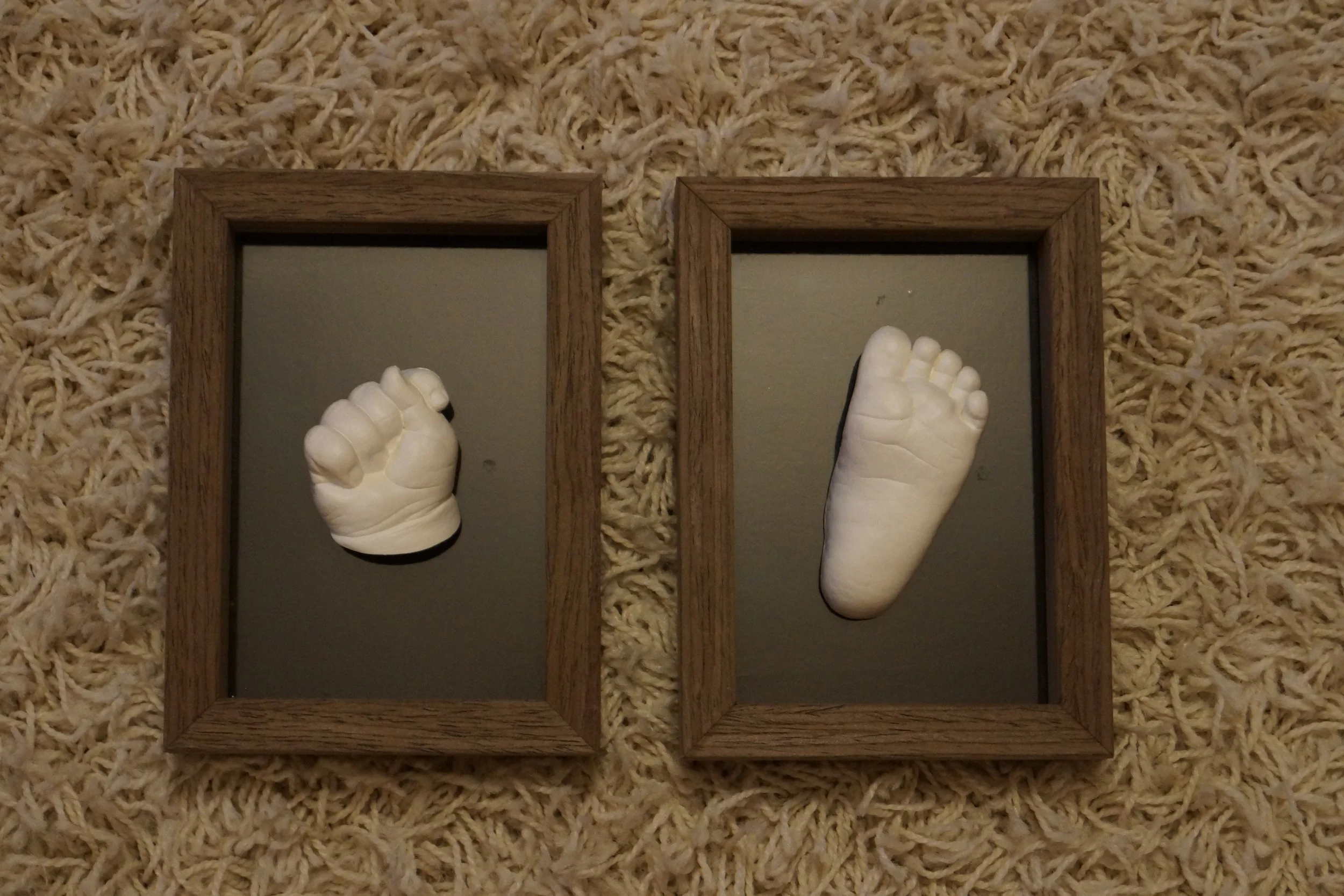 Zwei kleine Kinderfüße auf zwei gegenüberliegenden Spiegeln, die in einem Holzrahmen auf einem Teppich liegen.