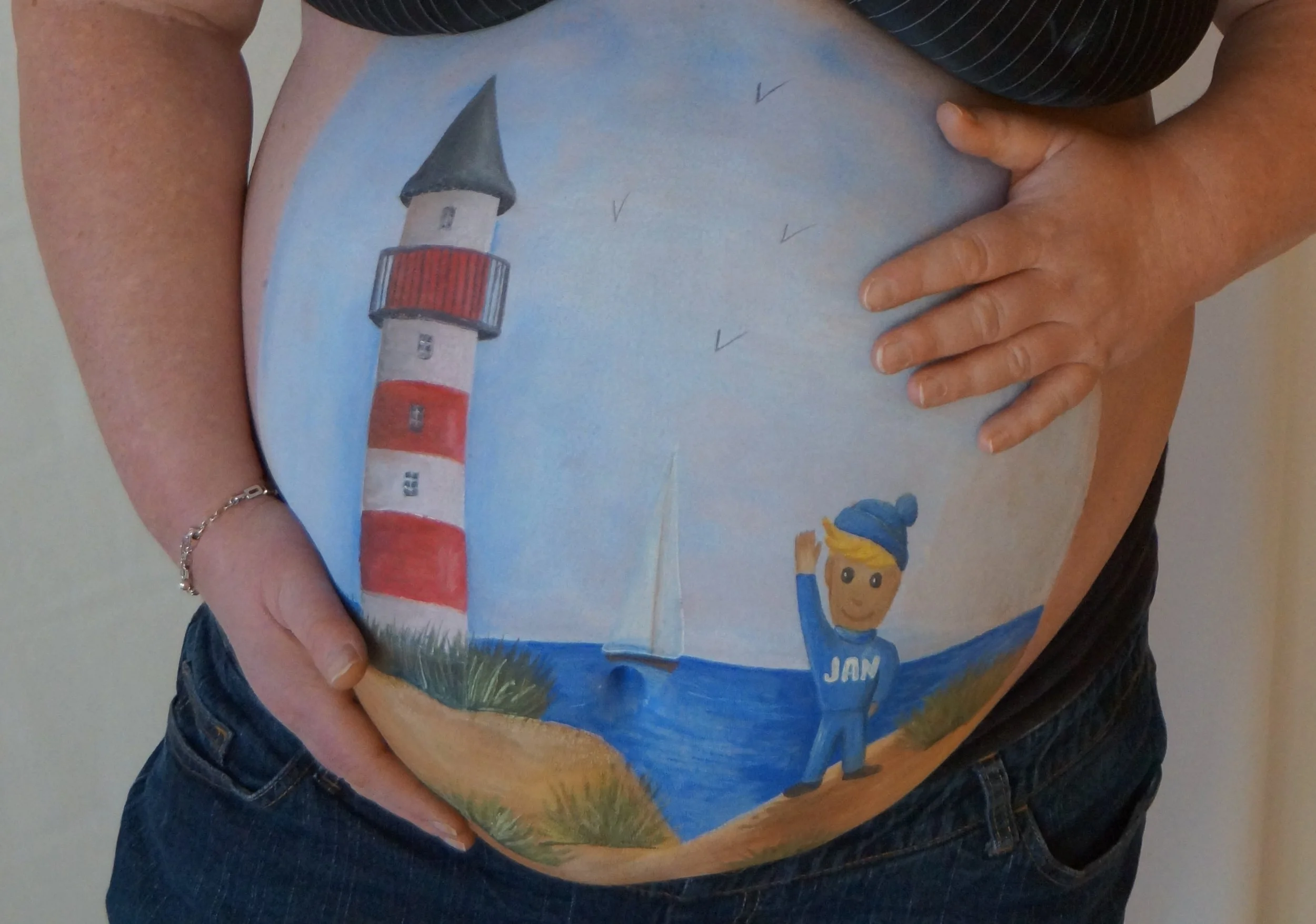 Ein Bauch mit einem handgemalten Bild eines Leuchtturms, einer Meerjungfrau und einem Vogel, dazu die Unterschrift "JAN".