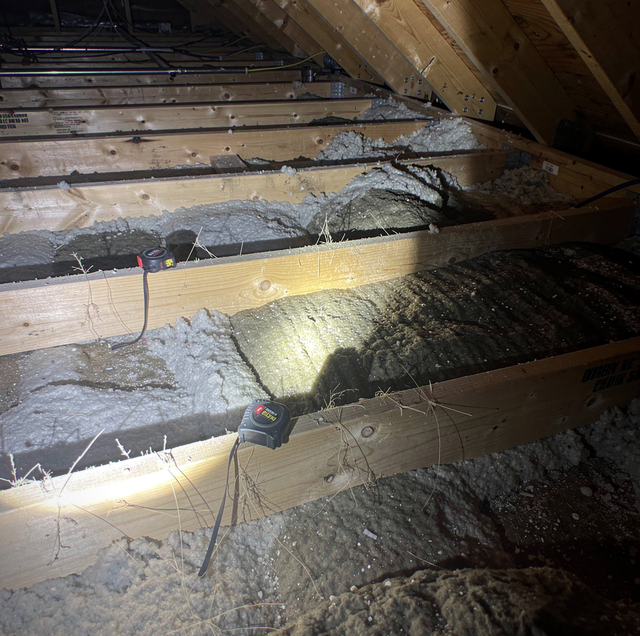 Wooden beams with insulation and electrical cables in an attic space.