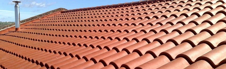 Close-up of a terracotta tile roof with a chimney on top, under a clear blue sky.