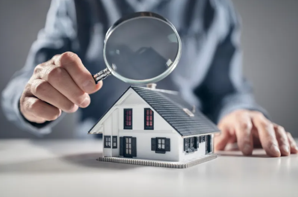 Person holding a magnifying glass over a miniature house.