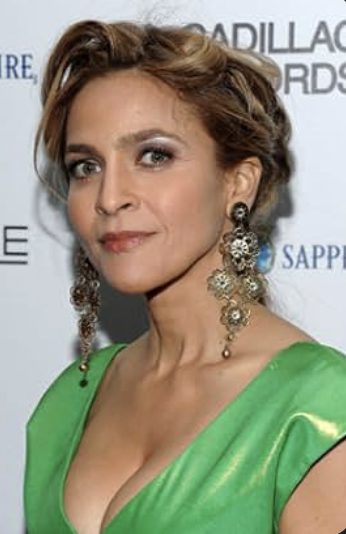 A woman with short, styled hair wearing a green dress with a deep neckline and large, ornate earrings at an event.