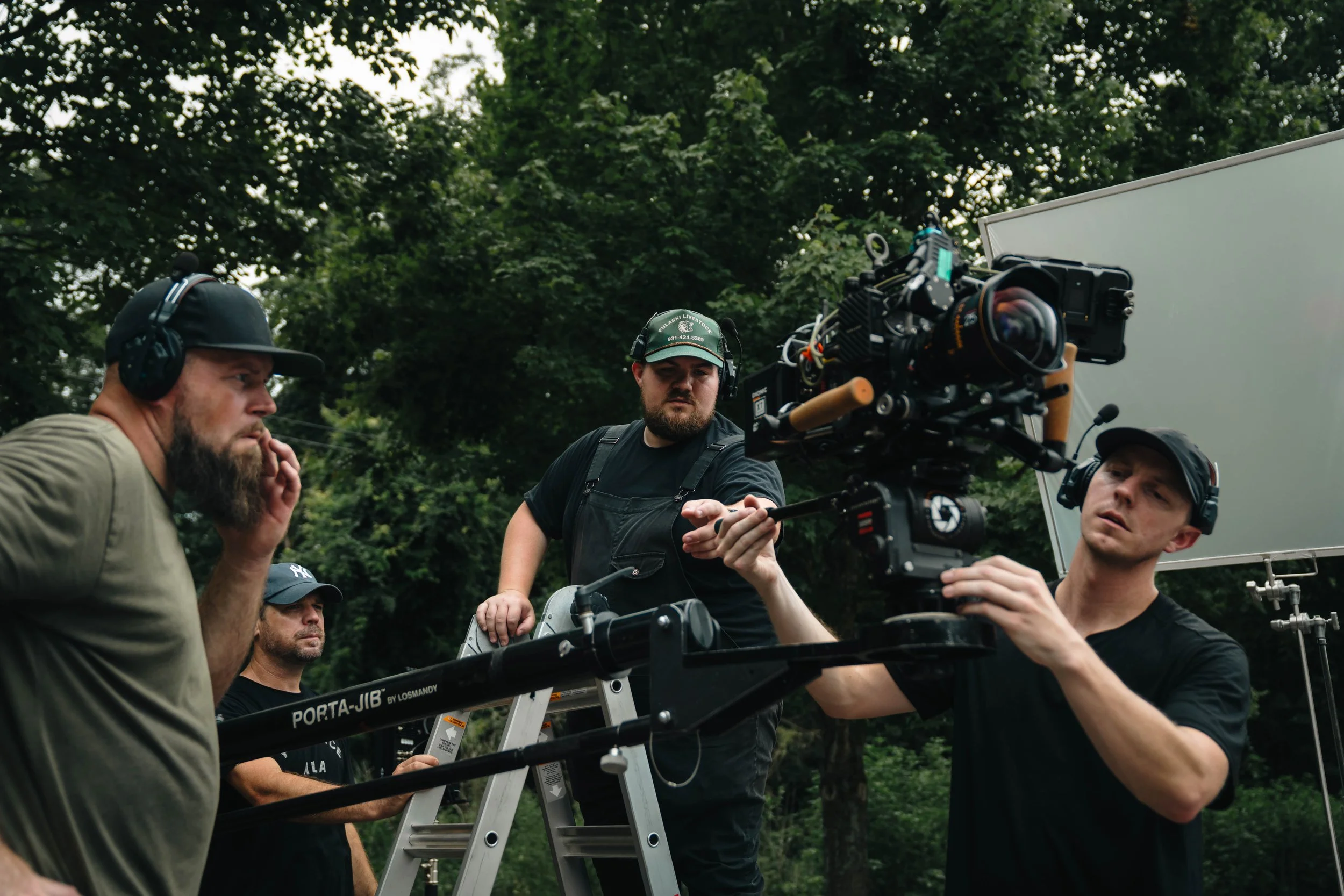Film crew working outdoors to set up a camera, with trees in the background.
