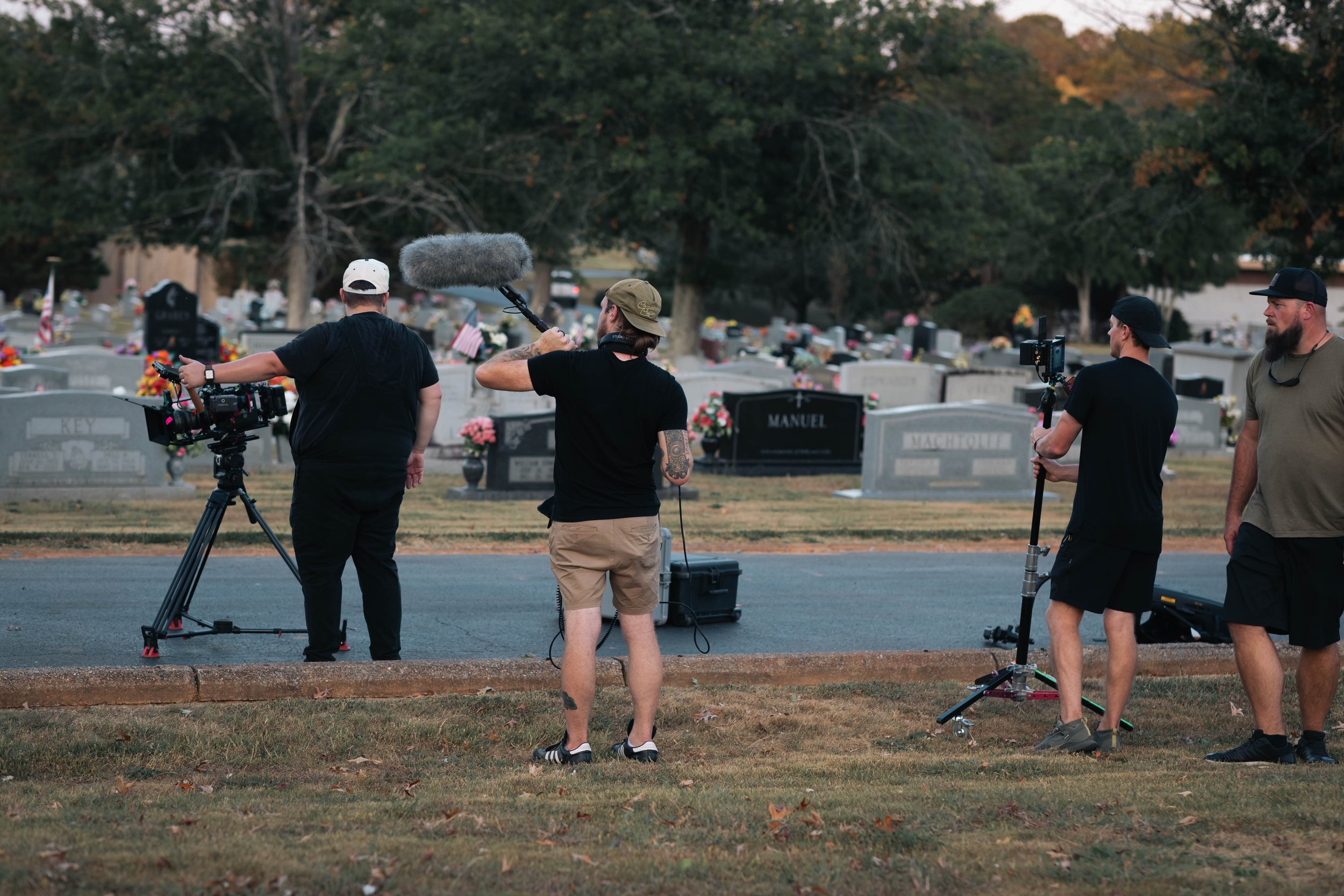 Film crew filming at a cemetery, with multiple crew members setting up cameras and audio equipment.