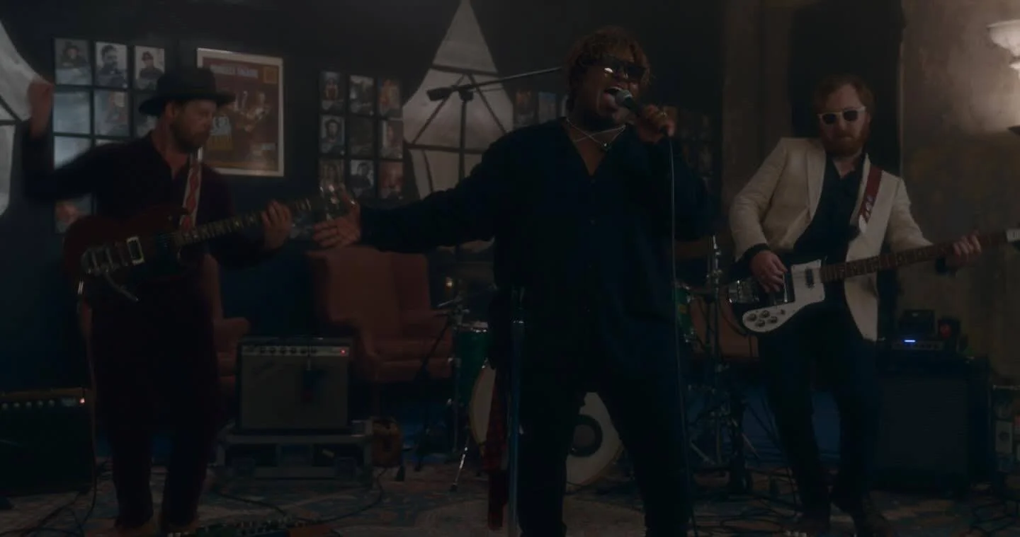 A band performing music in a dimly lit room with three members playing guitars and singing into a microphone.