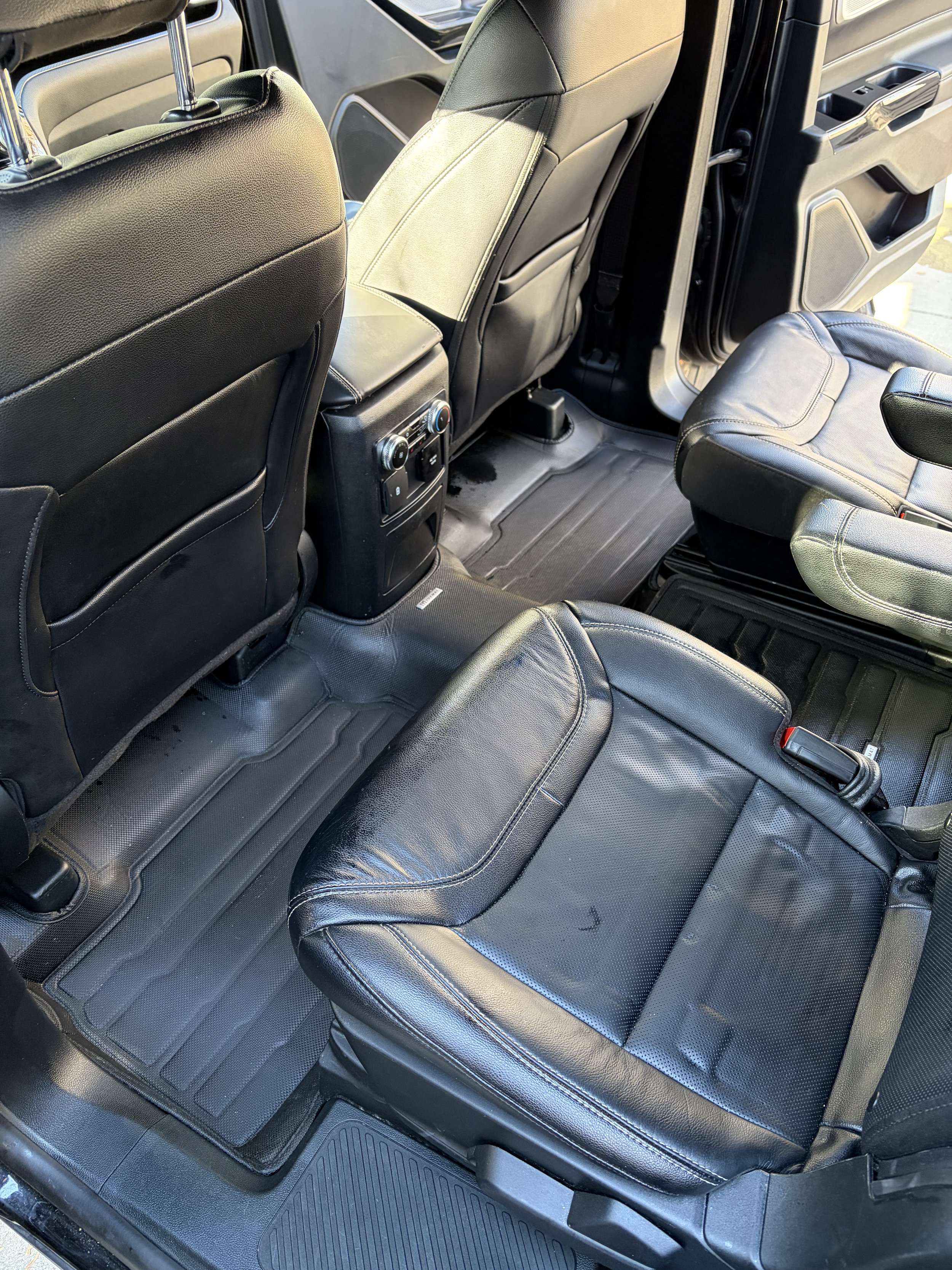 Interior of a vehicle showing the back seats and floor area, with black leather seats and rubber floor mats.