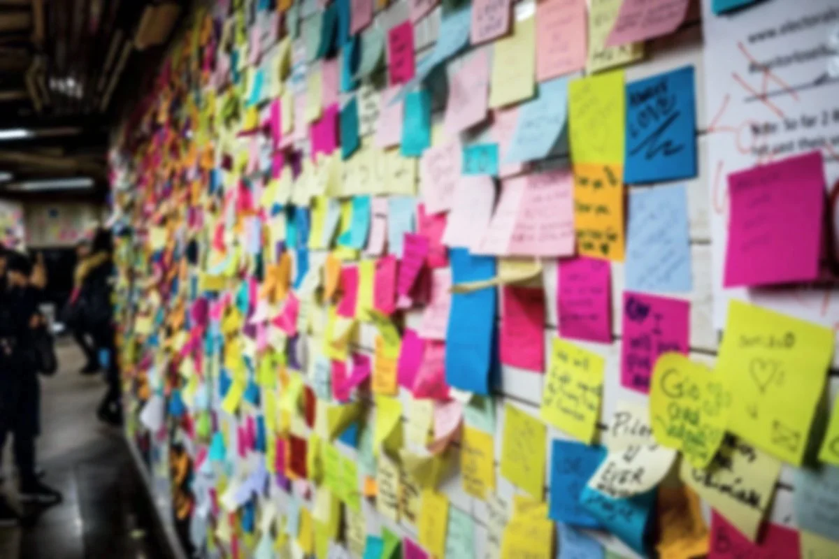A wall covered with colorful sticky notes and handwritten messages, with some people standing nearby.