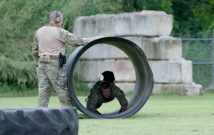 Military working dog and handler training with a large pipe in an outdoor setting.