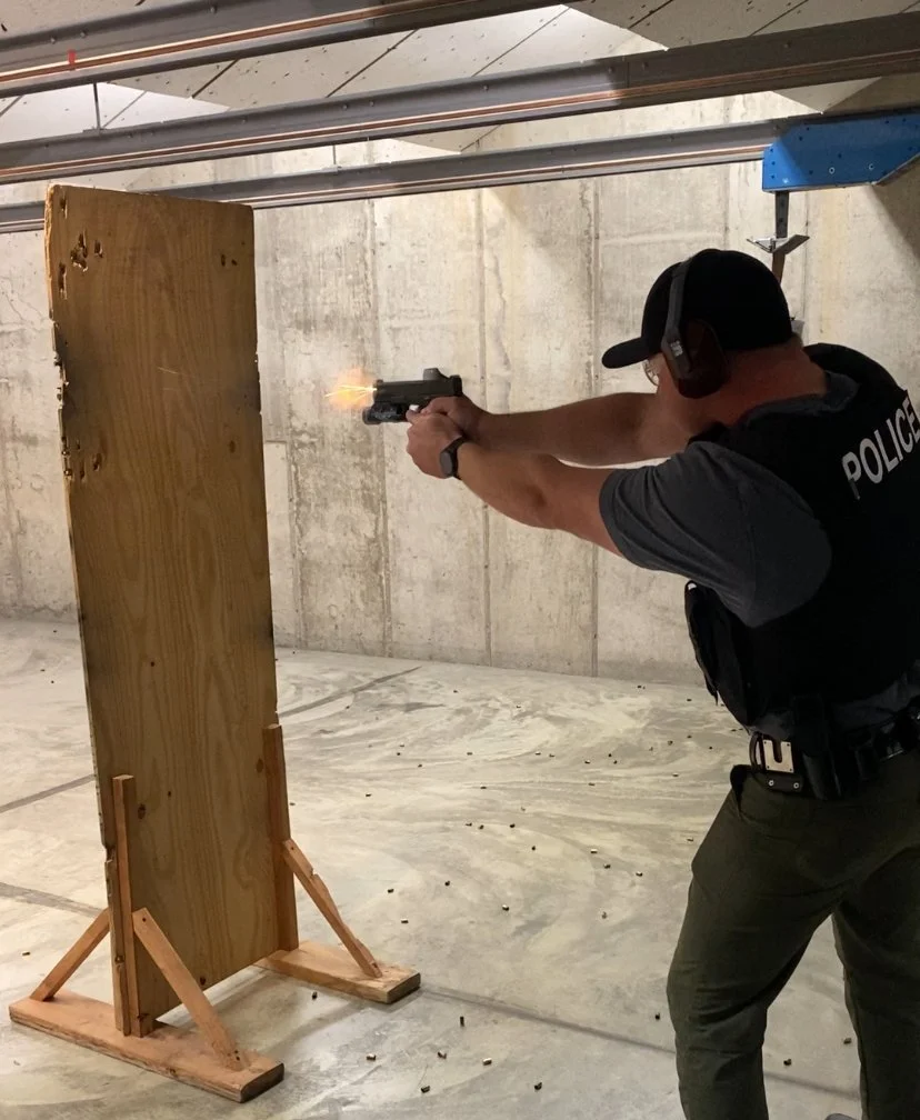 A police officer practicing firearms shooting at an indoor range, firing a handgun at a wooden target.
