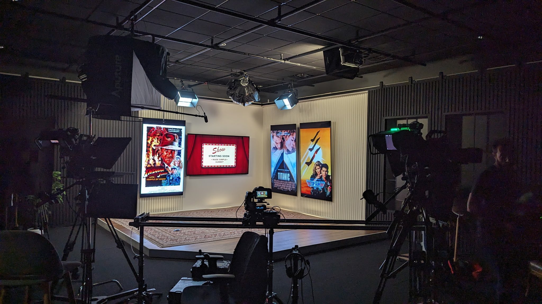 Television studio with cameras, lights, and screens displaying movie posters for Indiana Jones, Titanic, and Top Gun.