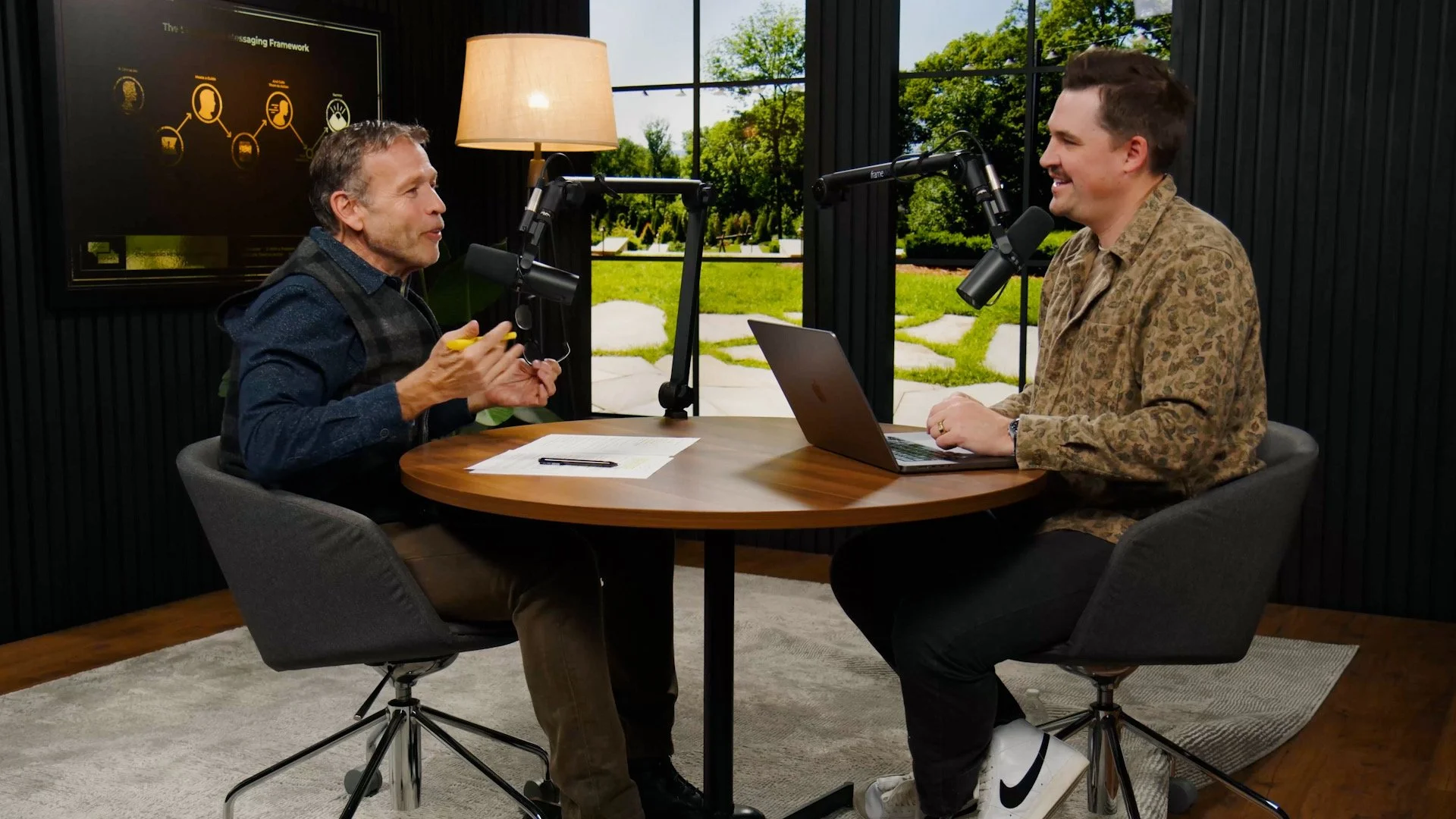 Two men having a conversation in a podcast studio with microphones, a laptop, and a large window showing trees outside in the new Donald Miller studio.