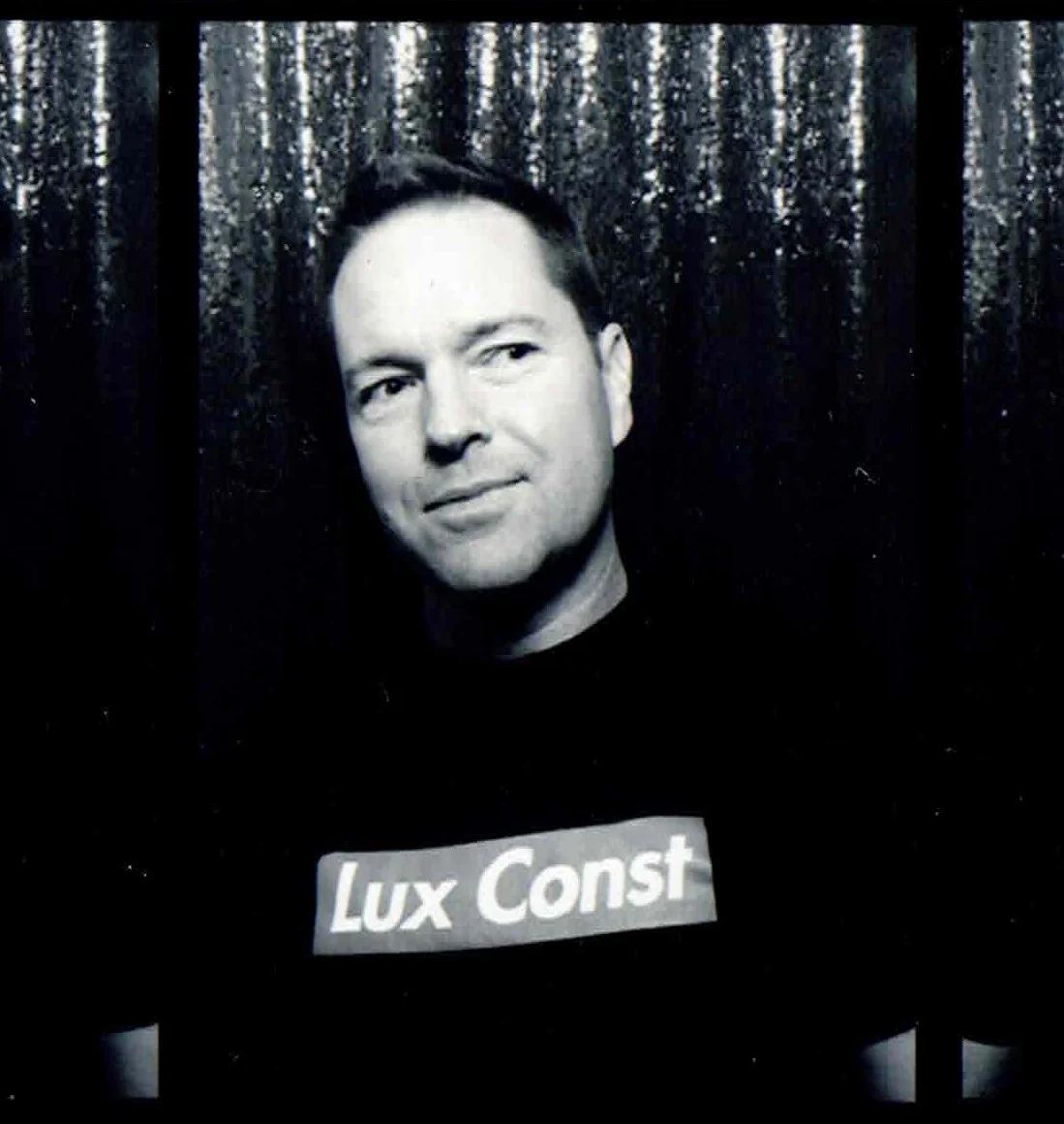 Black and white photo of a smiling man in a collared shirt, standing in front of a textured background.