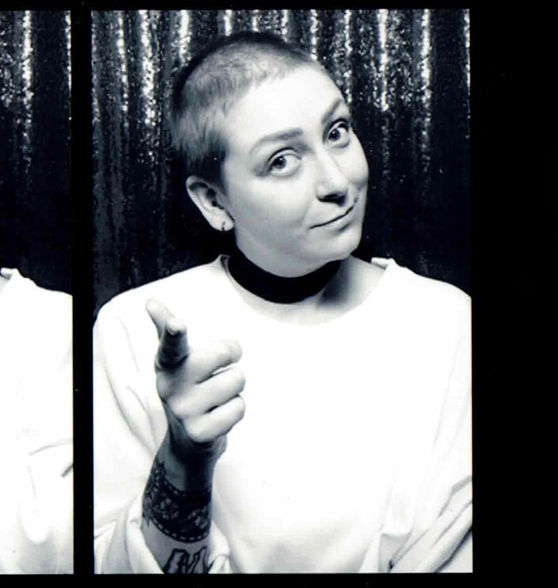 Black and white photo of a woman smiling and making a peace sign with her fingers, behind bars.