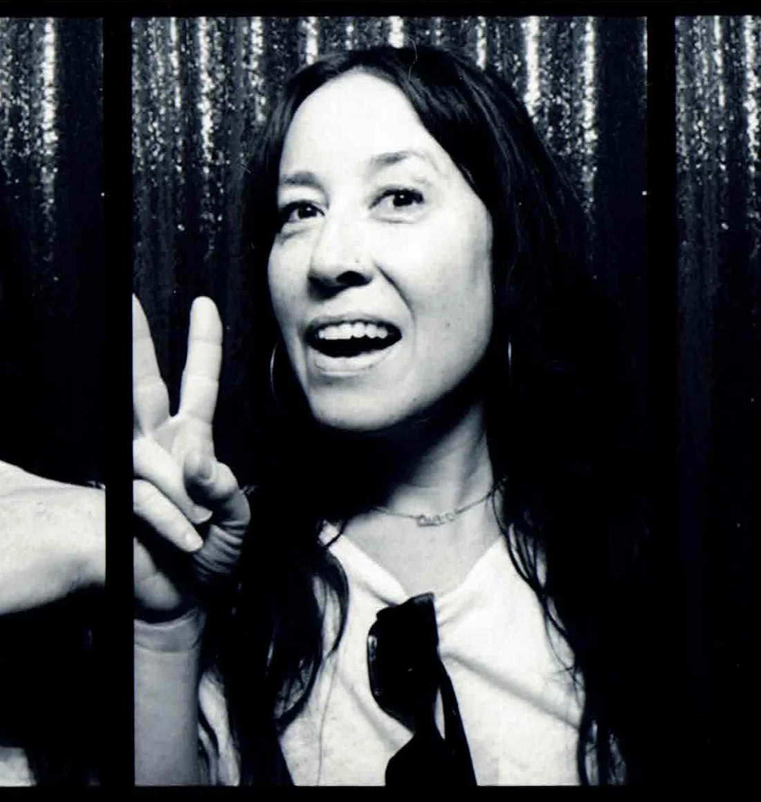 Black and white photo of a woman smiling and making a peace sign with her fingers, behind bars.