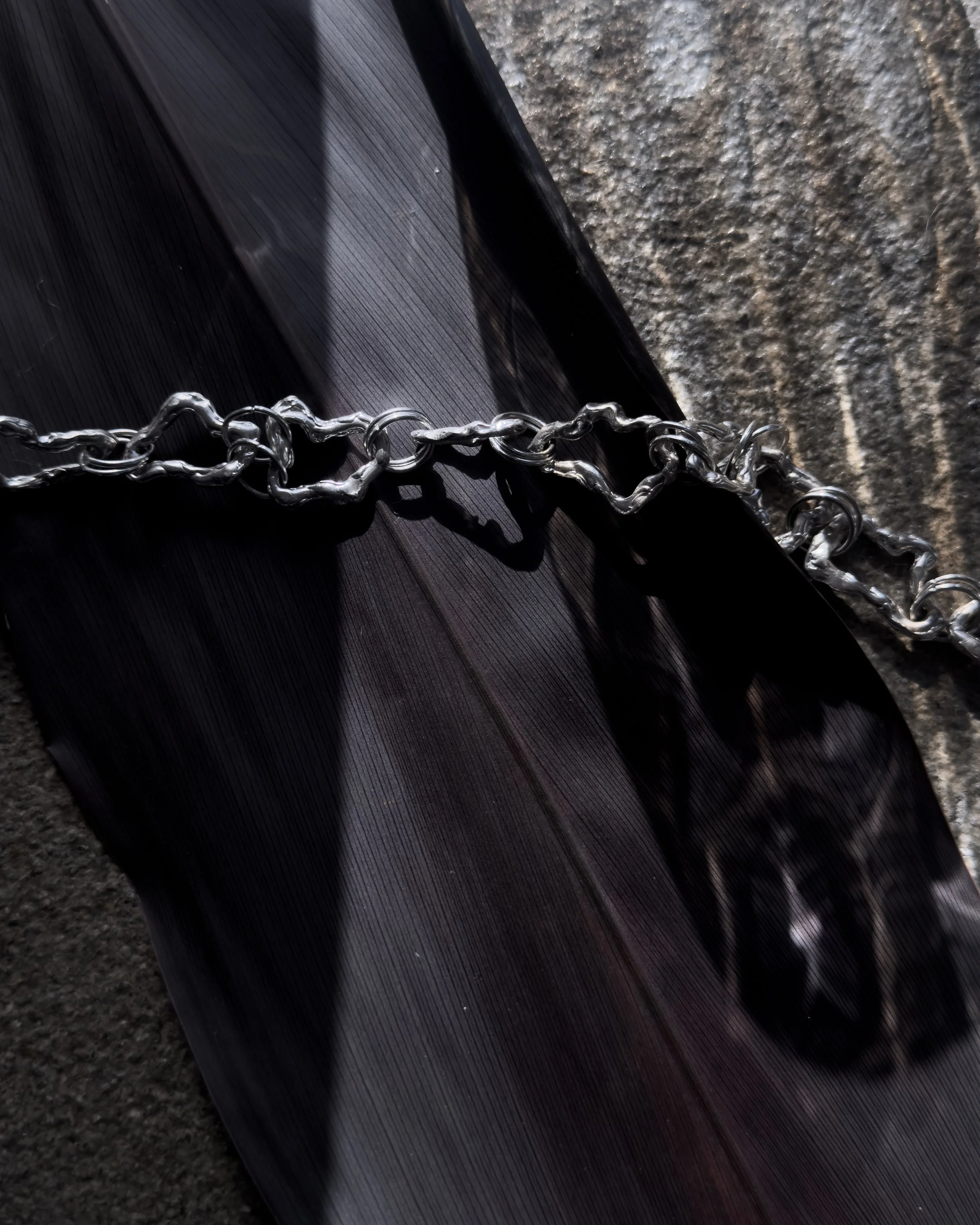 A close-up of a twisted metal chain lying on a dark, glossy surface, with part of a textured stone surface visible in the background.