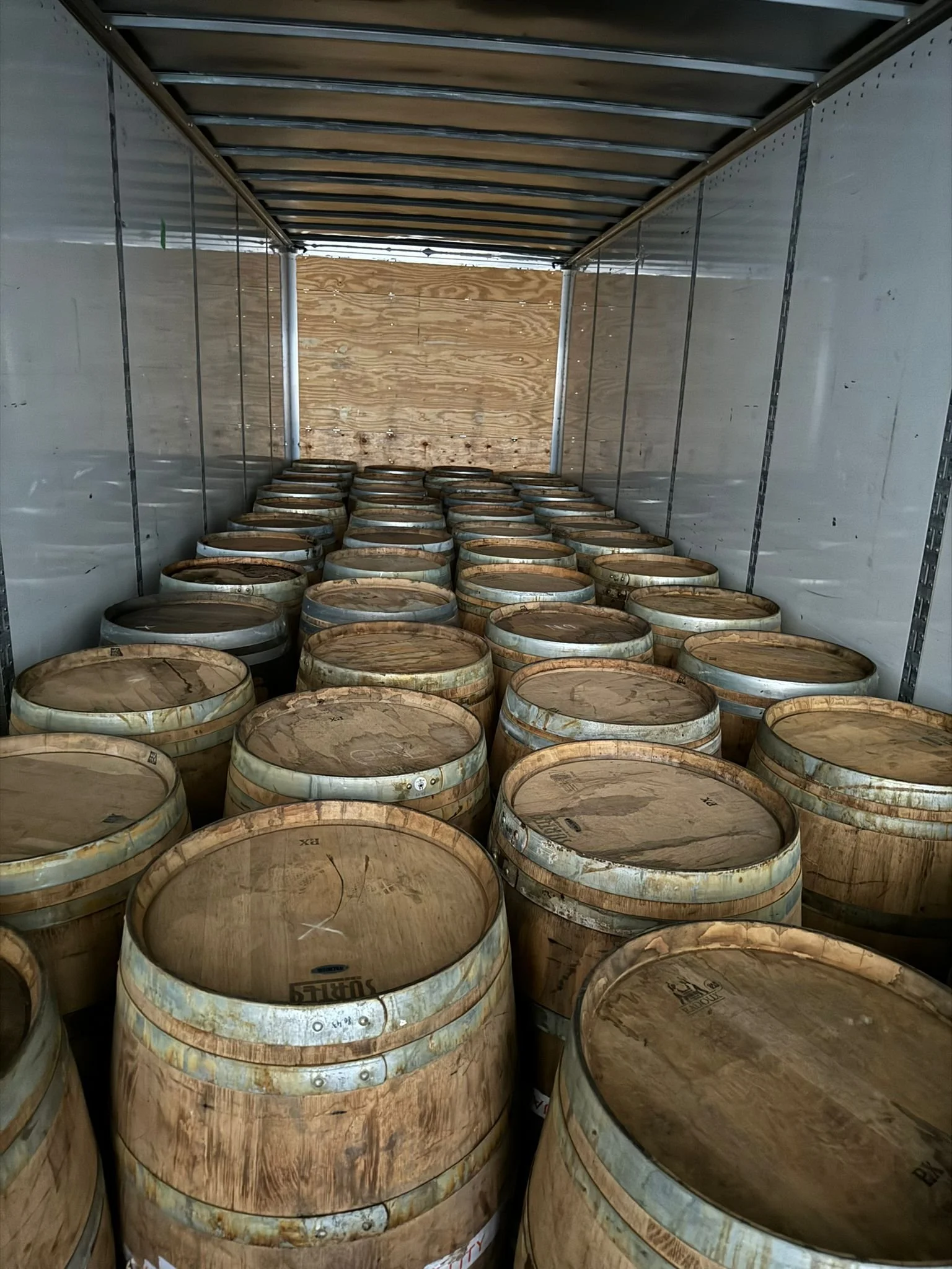 Wooden barrels stored inside a metallic truck or container.
