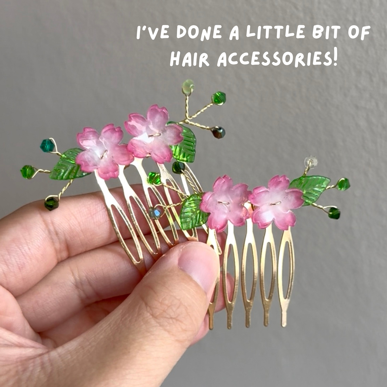 Hand holding a decorative hair comb adorned with pink flowers, green leaves, and colorful beads. Gray wall background.