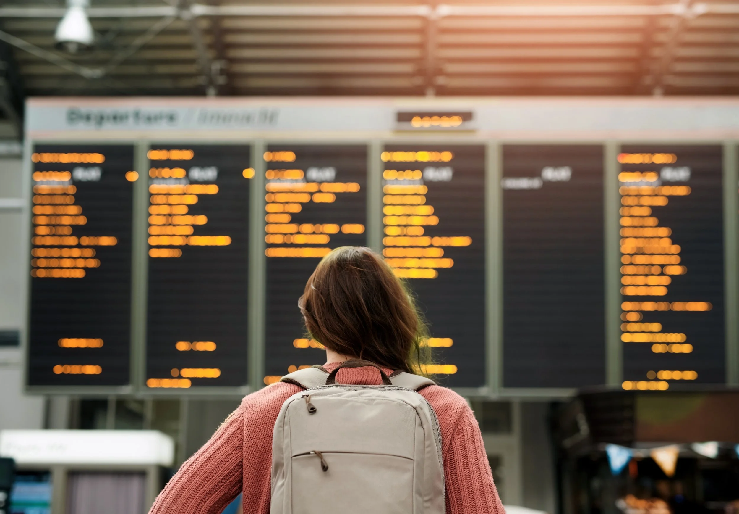 A woman with a backpack standing in front of a flight board
