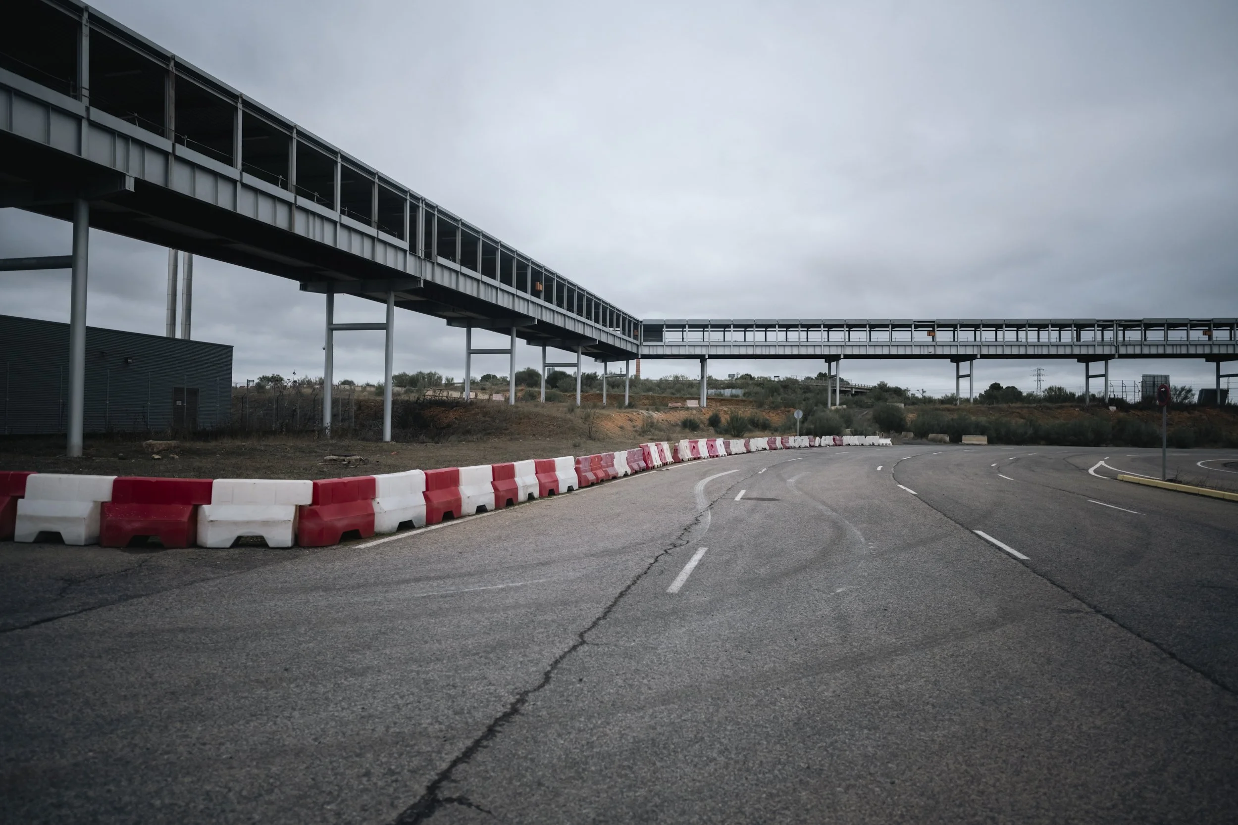 Red barriers, pale asphalt—an arrival path that ends before it begins.