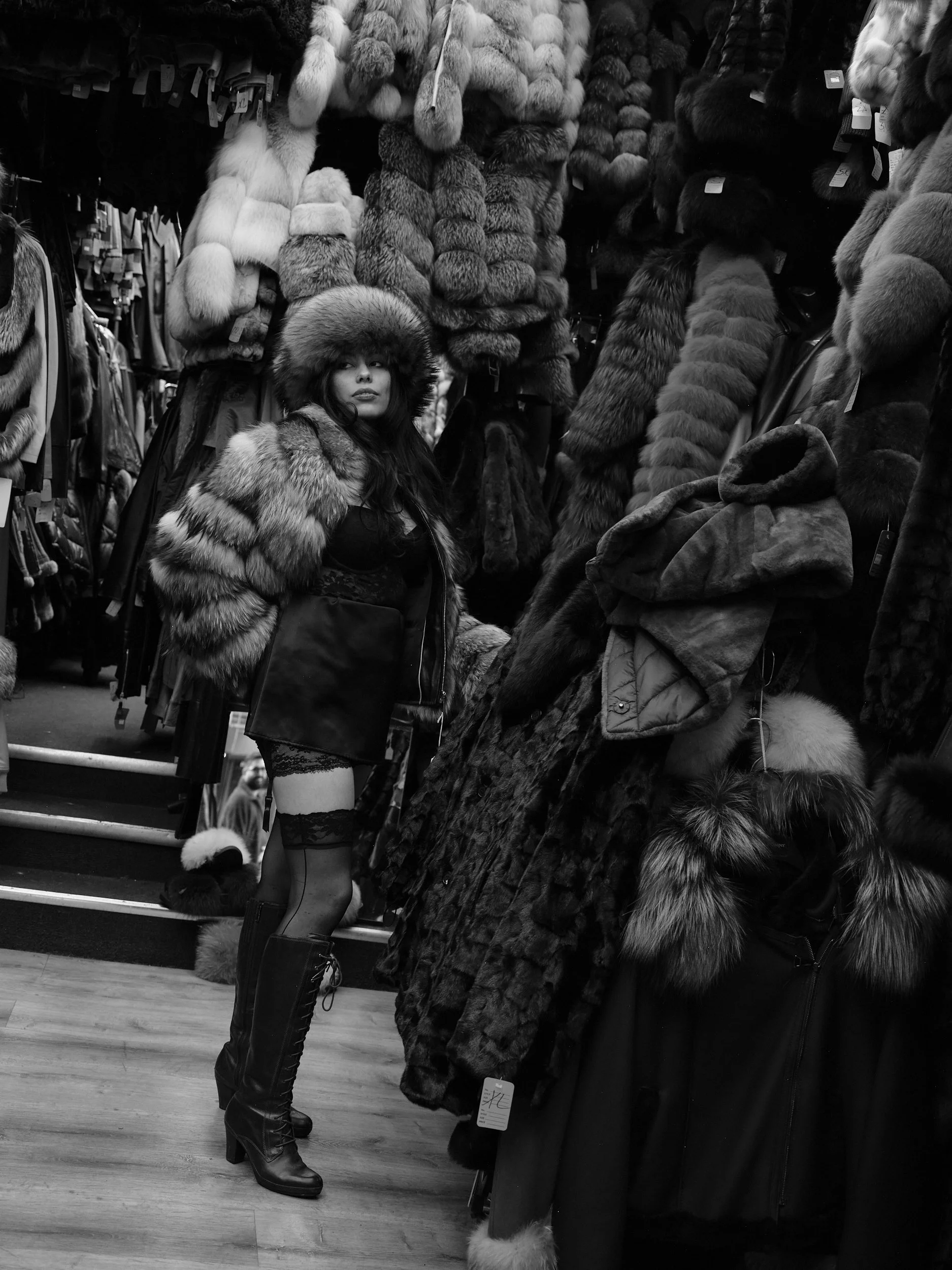 A woman in a fur hat and fur coat in a store aisle lined with fur hats and coats.
