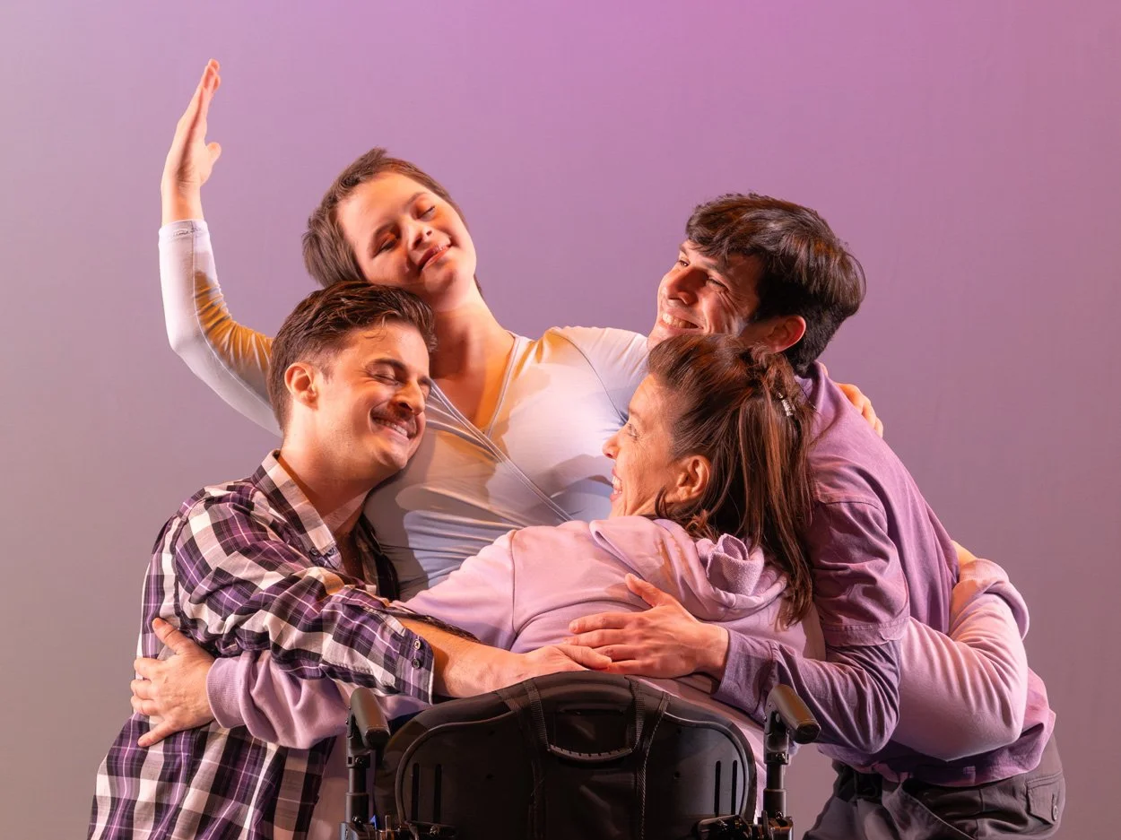 Born Dancing performance at Alvin Ailey, group of five happy people hugging and smiling together, one person in a wheelchair, dressed casually, against a purple wall.