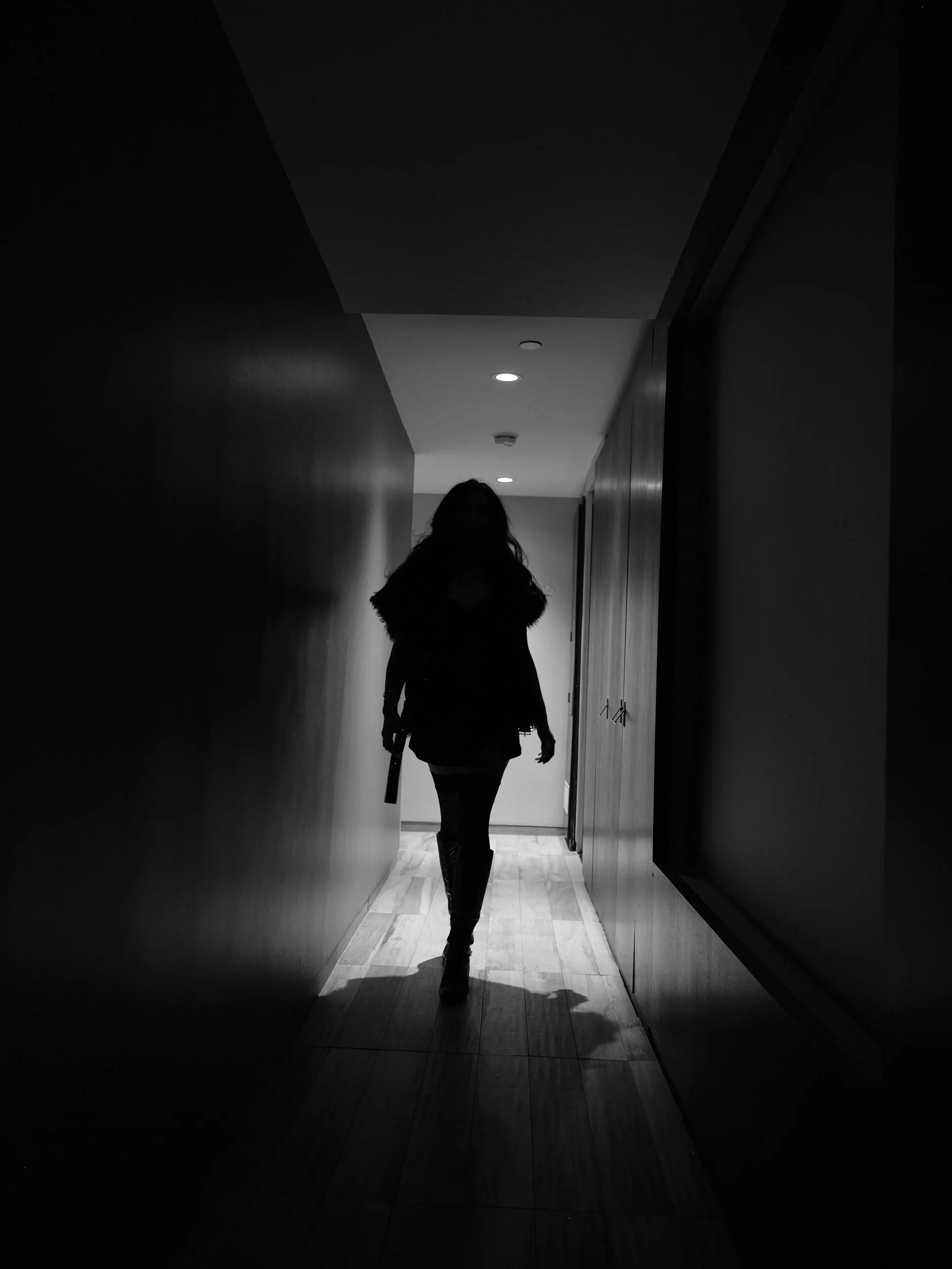 Silhouette of a woman walking down a dimly lit hallway with overhead lights.