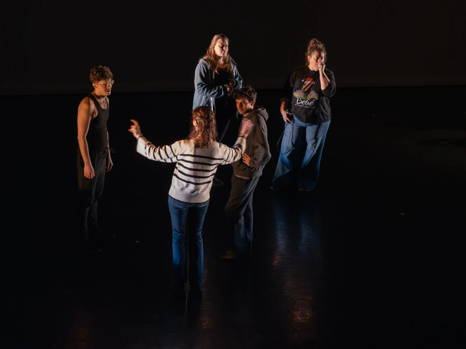 Five people standing in a circle on a dark stage, engaged in conversation - Born Dancing