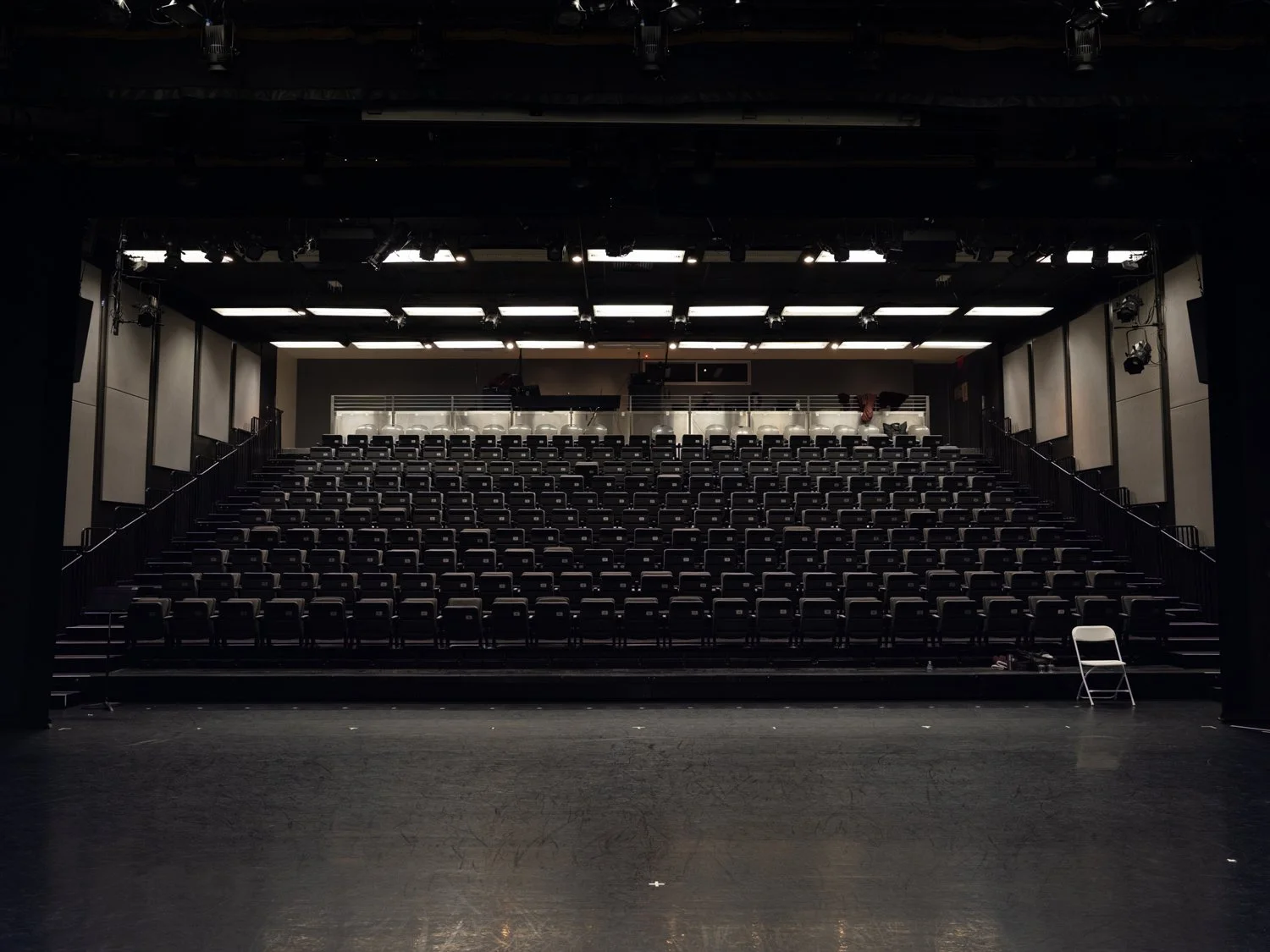 Empty theater stage at Alvin Ailey with black curtains, chairs, and lighting equipment, viewed from the stage.