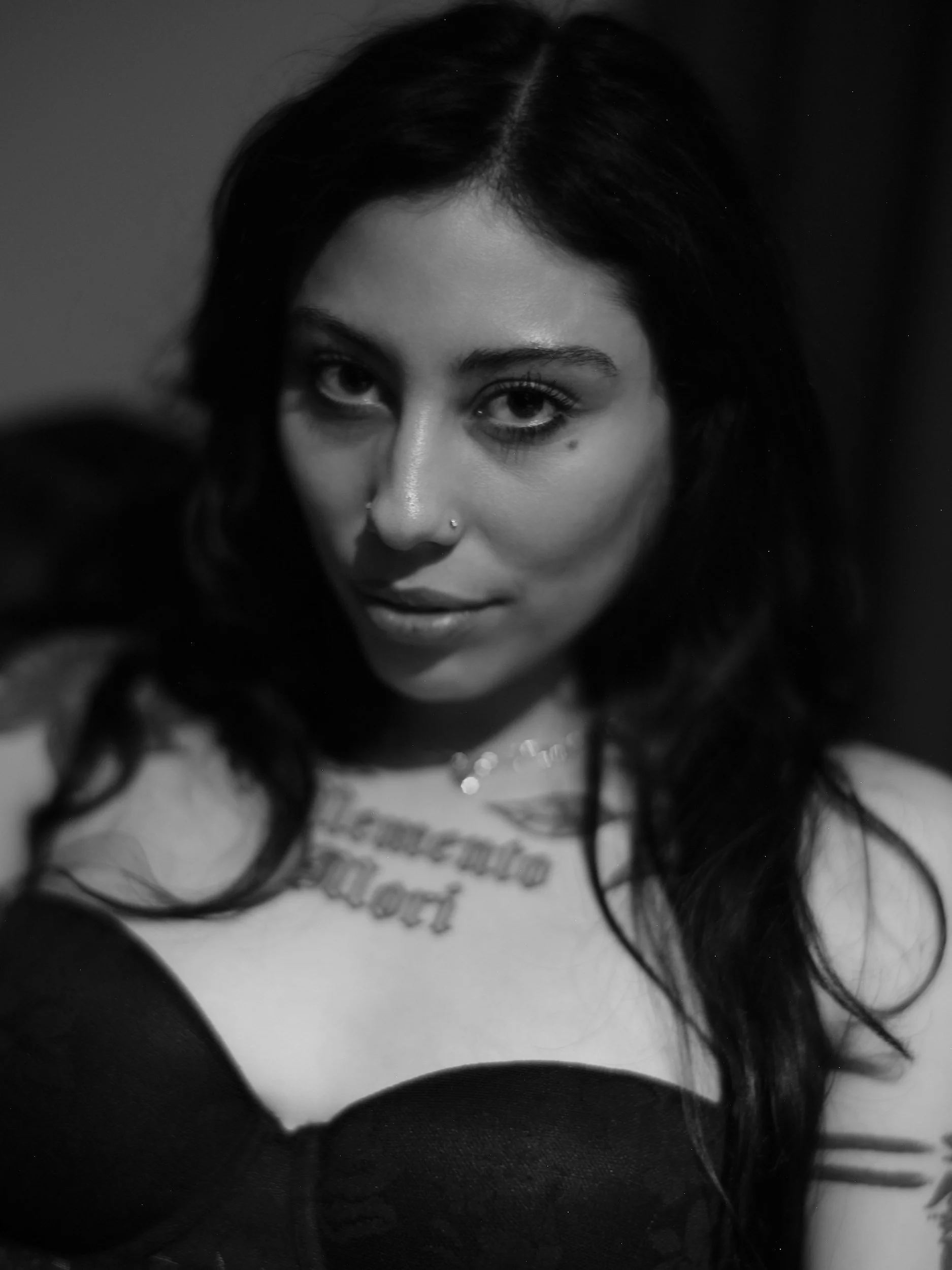 Black and white portrait of a woman with dark hair, tattoos, and facial piercings.