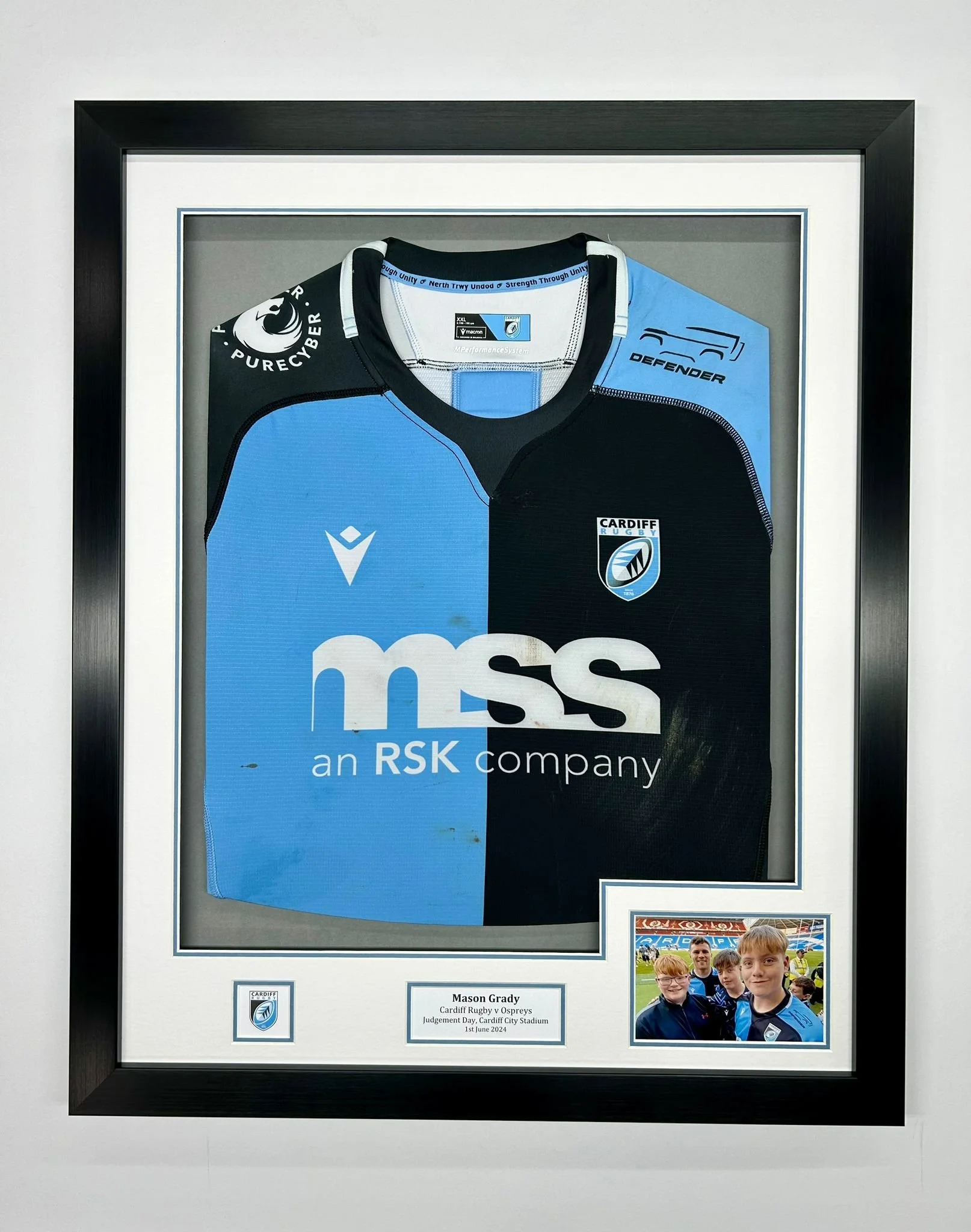 Framed Cardiff Rugby jersey with team logos and sponsors, and a small photo of young fans at a rugby stadium.