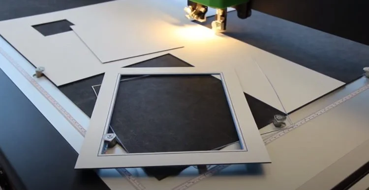 A sewing machine working on a piece of fabric with a square embroidery hoop attached.