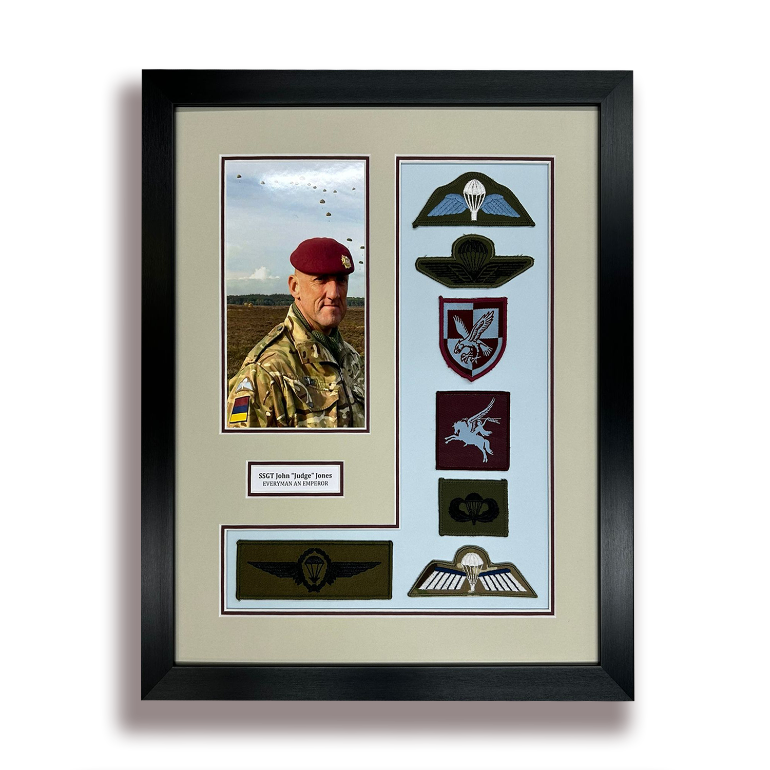 Framed military memorabilia display featuring a photograph of a soldier in camouflage uniform with a maroon beret, a nameplate that reads 'SSGT John 'Judge' Jones, Everyman an Emperor,' and various embroidered patches representing military units and honors.