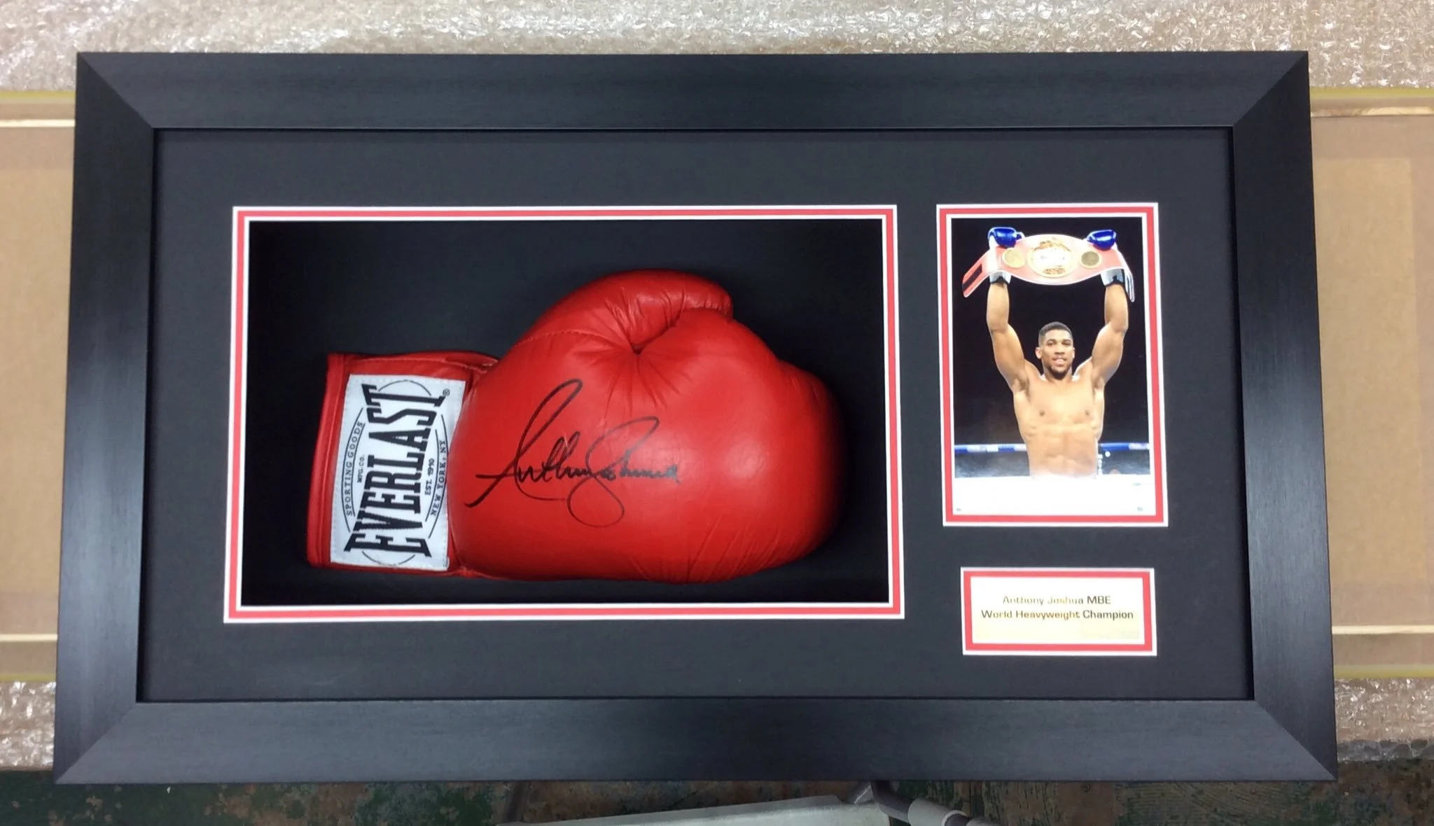 Framed display of a red boxing glove with a signature, a package of Everlast boxing wraps, and a photograph of Anthony Joshua holding a championship belt