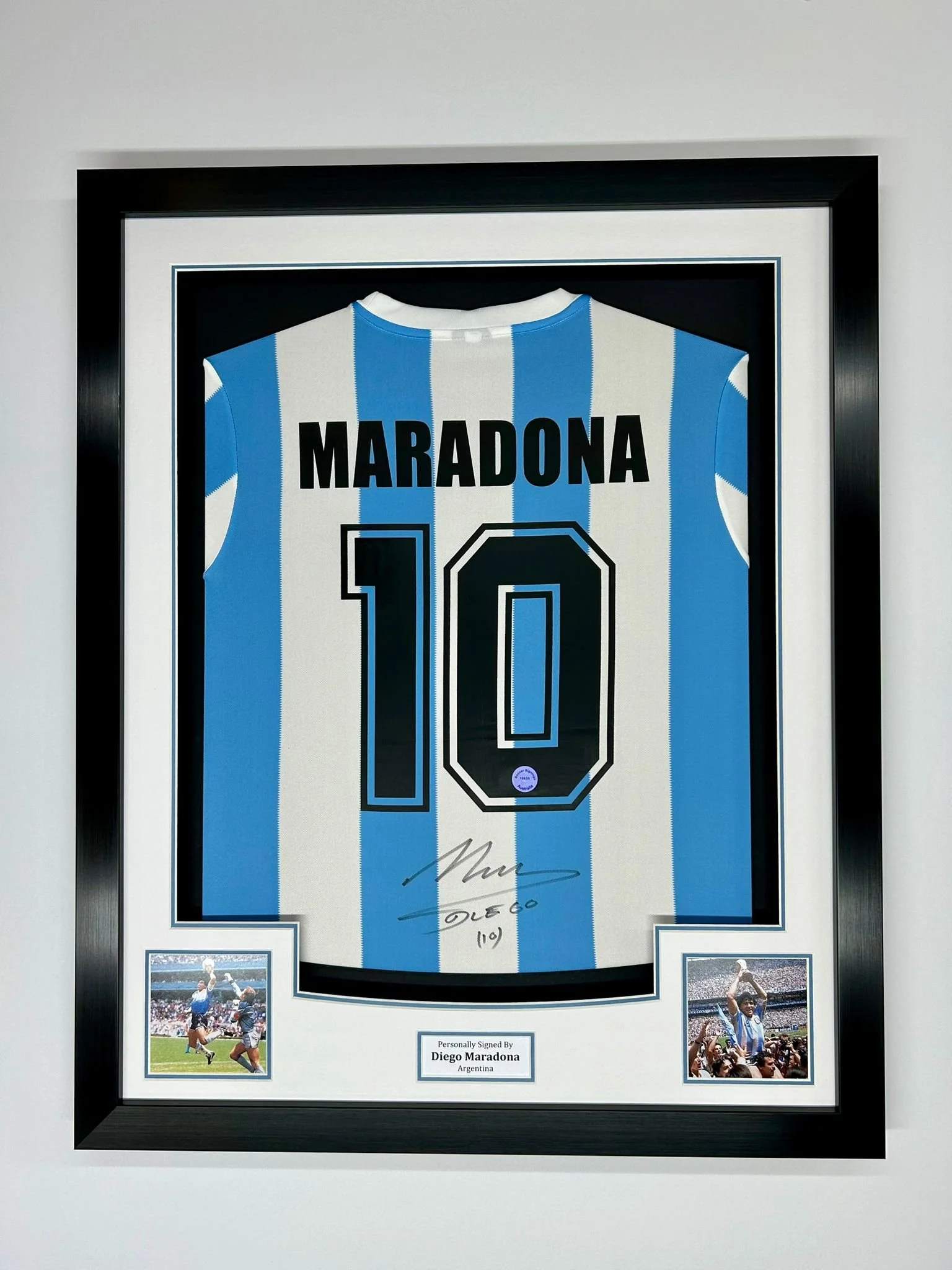 Framed signed Diego Maradona Argentina soccer jersey with black and white vertical stripes, the number 10, and photos of Maradona playing soccer below the jersey.